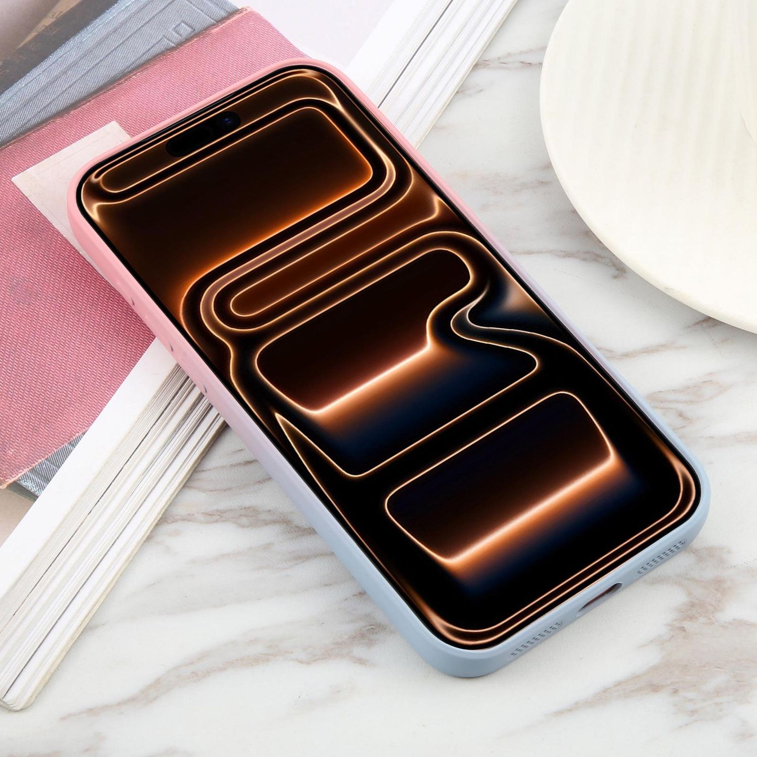 Ein Smartphone in einer hellblauen und rosa Hülle liegt auf einer Marmoroberfläche, neben Büchern und einem weißen Teller.