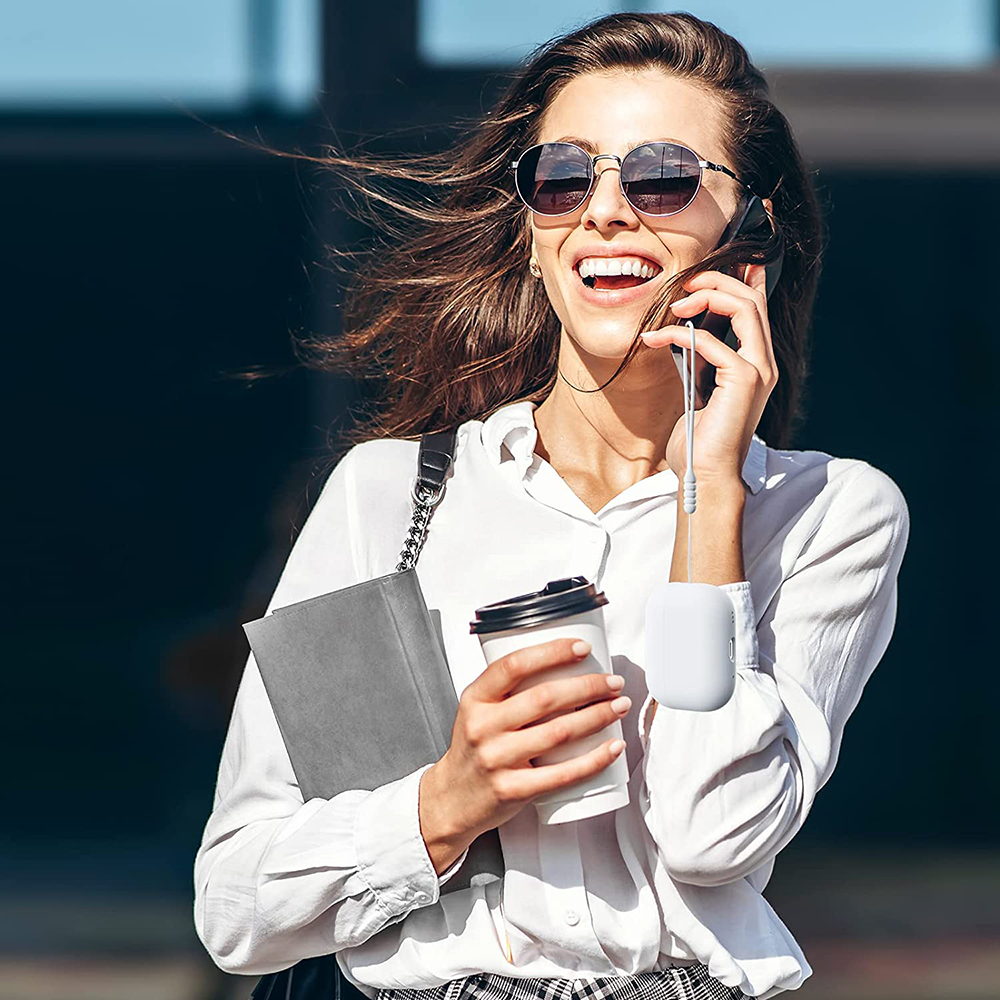 Frau mit Sonnenbrille telefoniert, hält Kaffee und ein Buch. Sie lächelt und trägt ein weißes Hemd.