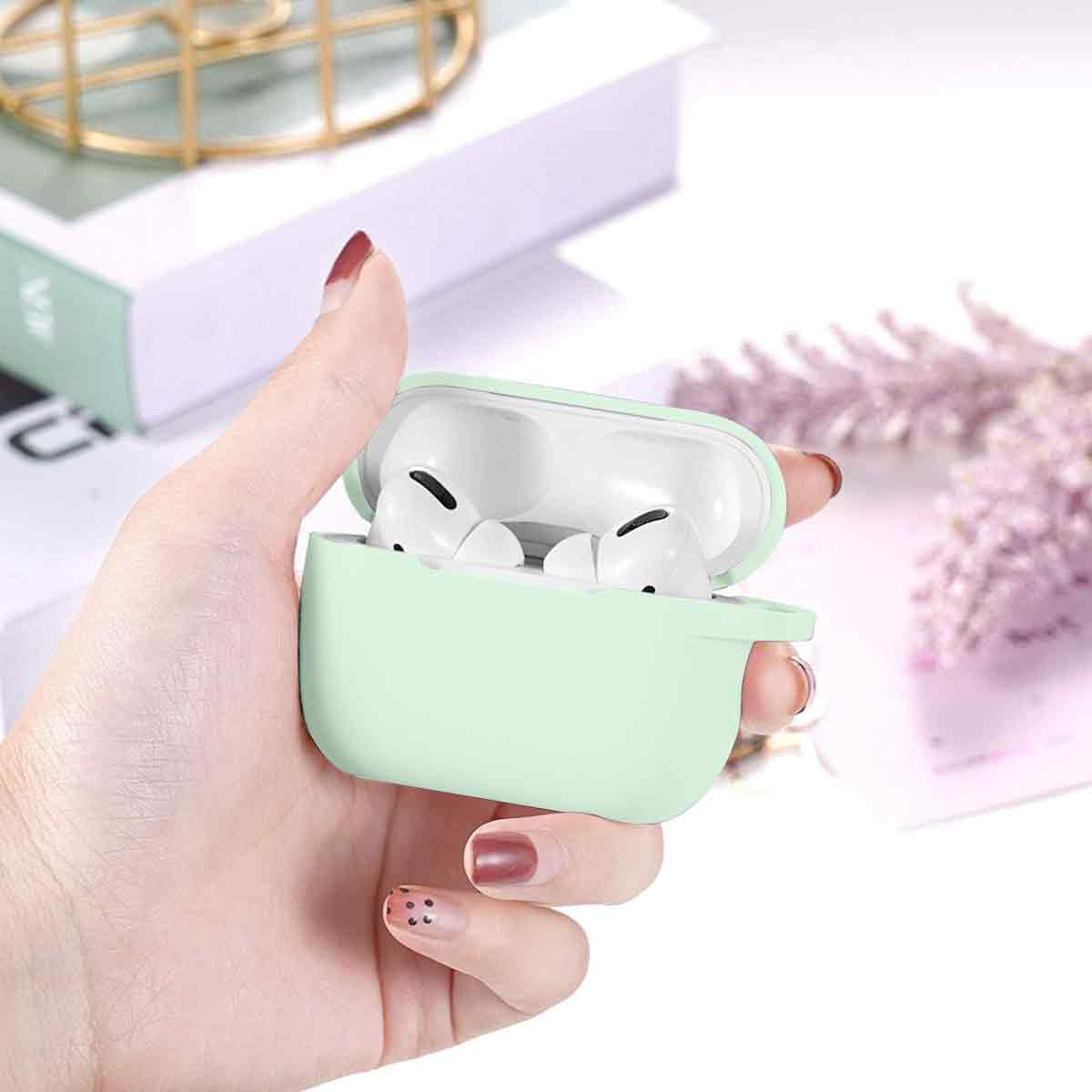 Eine Hand hält eine mintgrüne AirPods-Hülle mit weißen Ohrhörern. Ein Buch und Blumen sind im Hintergrund. Die Fingernägel sind rot.