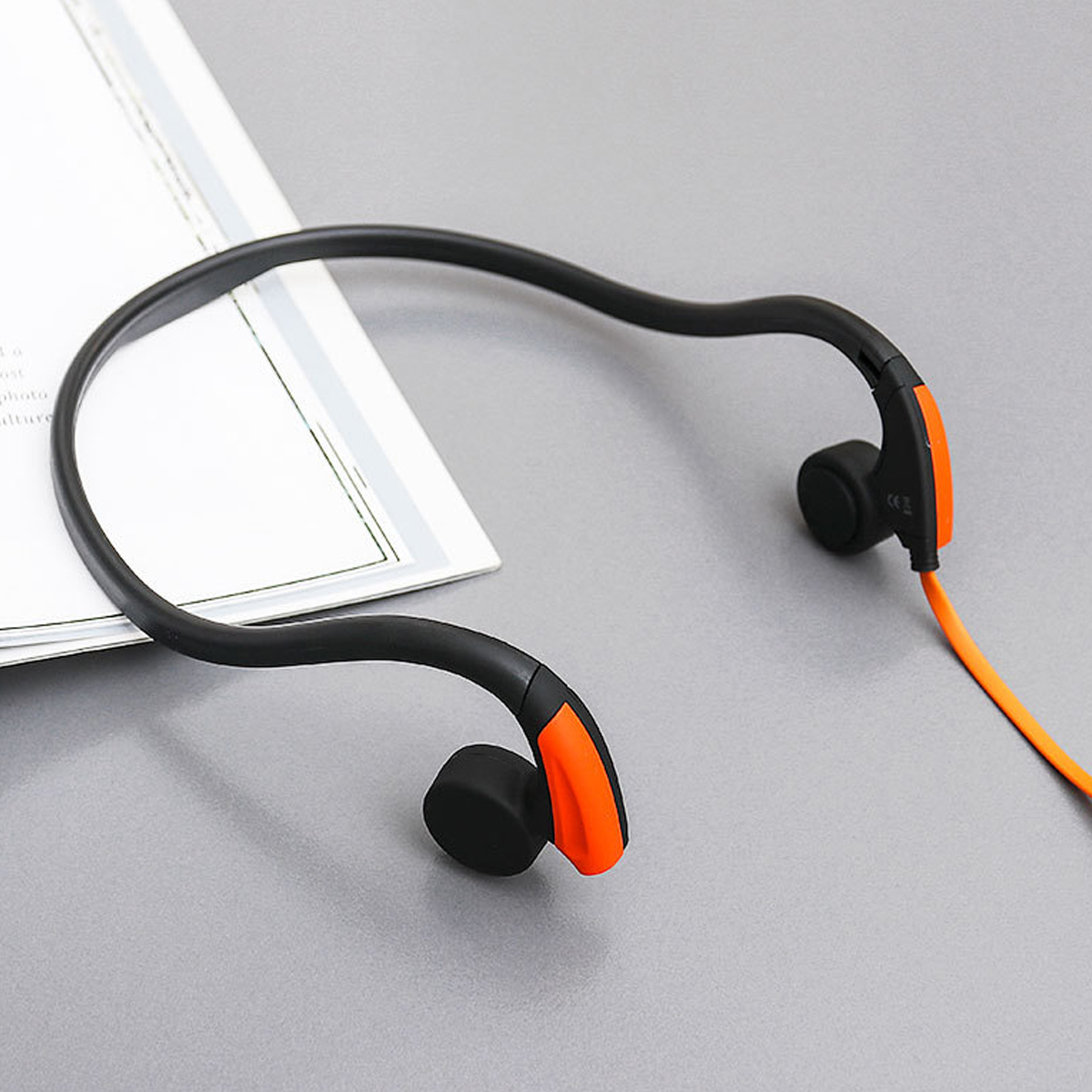 Schwarze und orangefarbene kabellose Kopfhörer auf grauer Oberfläche mit weißem Papier. Das Kabel ist orange.