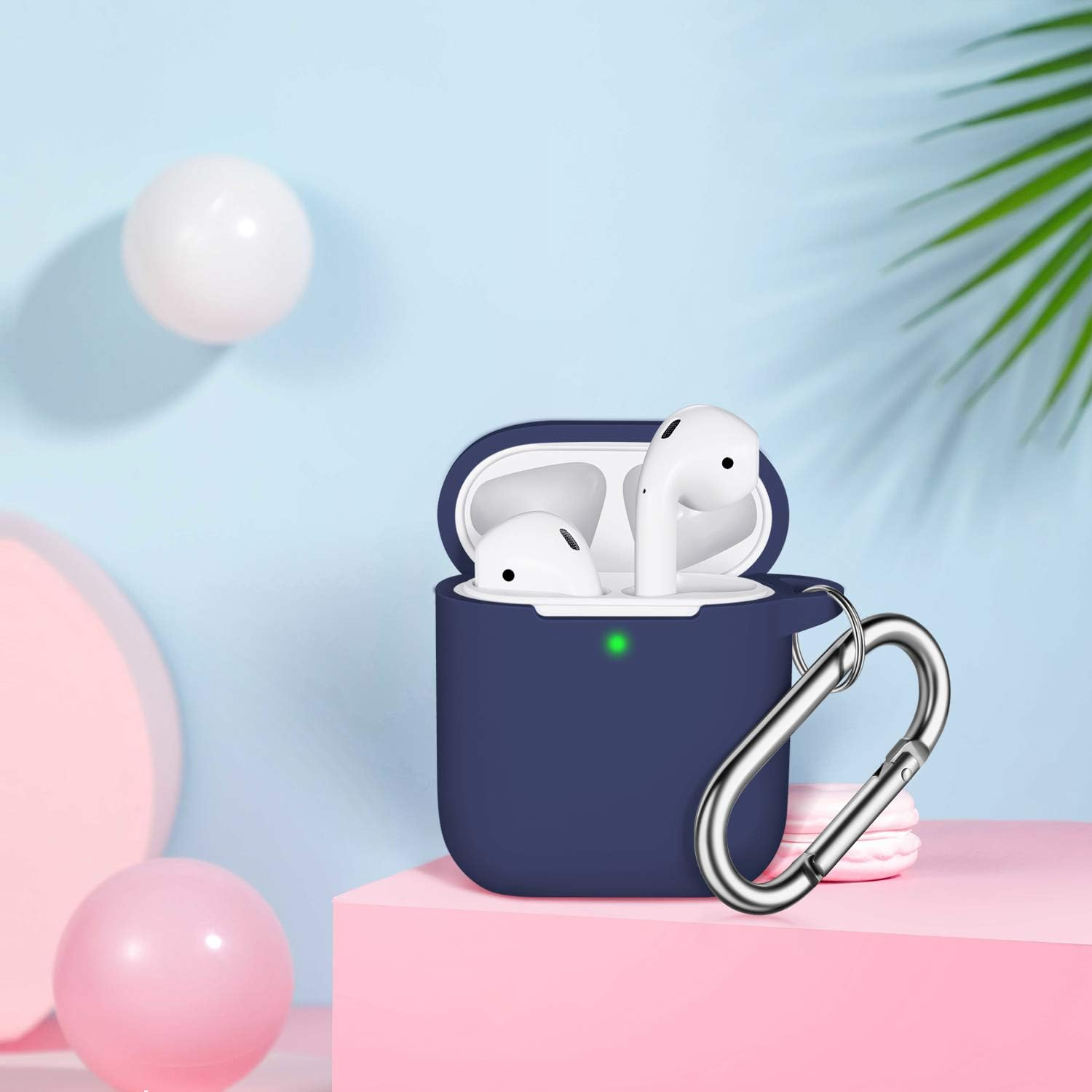 Marineblaues AirPods-Case mit weißen Ohrhörern, silbernem Clip, auf rosa Oberfläche. Rosa und weiße Kugeln im Hintergrund.
