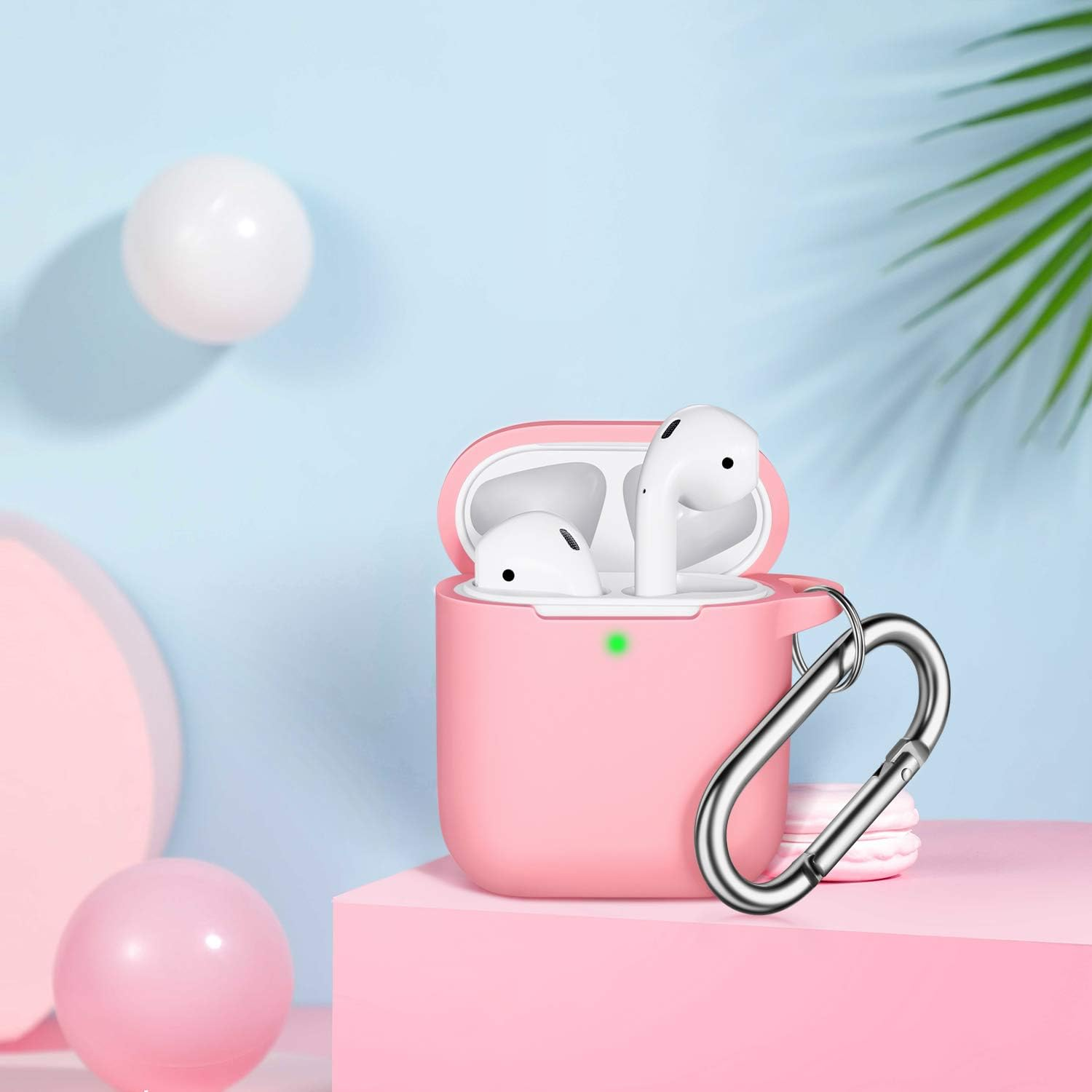 Rosa AirPods in einem rosa Etui mit einem silbernen Karabinerhaken. Weiße und rosa Kugeln und ein blauer Hintergrund.