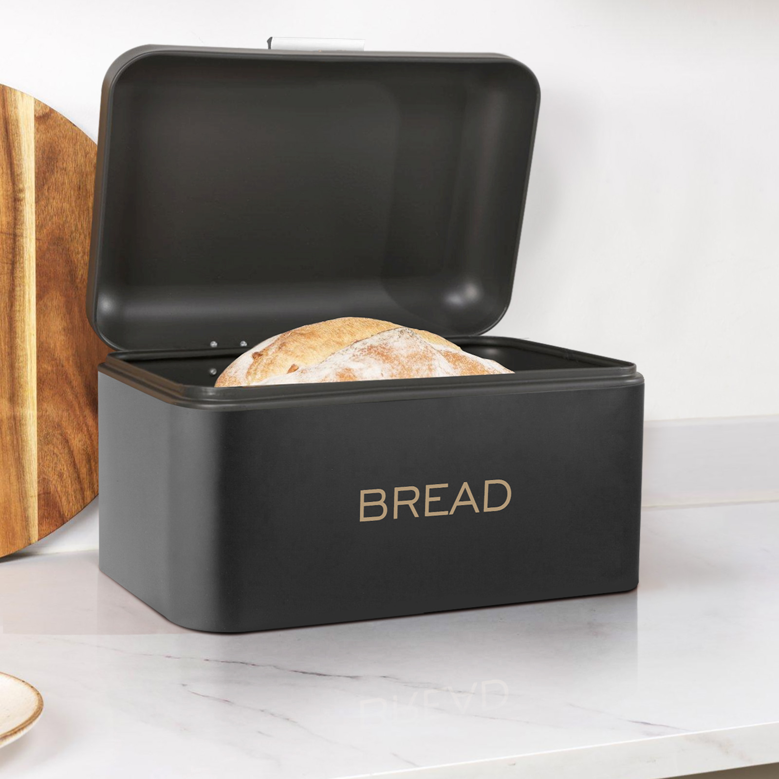 Schwarzer Brotbehälter mit offenem Deckel, enthält ein Brotlaib. Links ein Holzbrett.