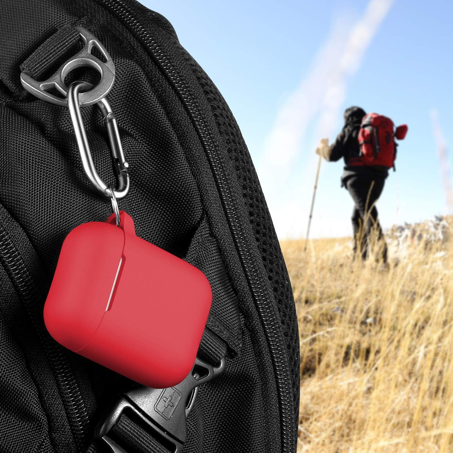 Ein rotes Etui mit Karabinerhaken ist an einem schwarzen Rucksack befestigt. Im Hintergrund wandert eine Person.