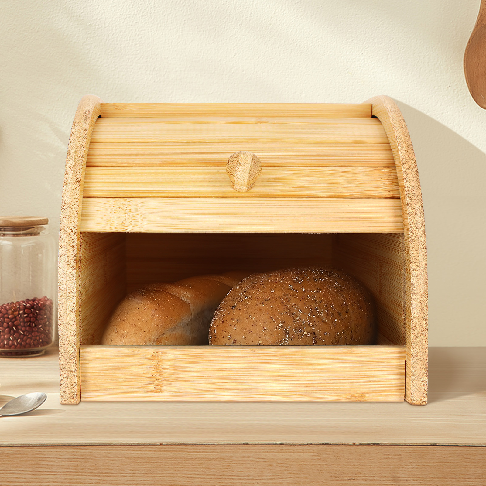 Ein hölzerner Brotkasten mit zwei Brotlaiben darin. Links steht ein Glas Bohnen, davor liegt ein Löffel.
