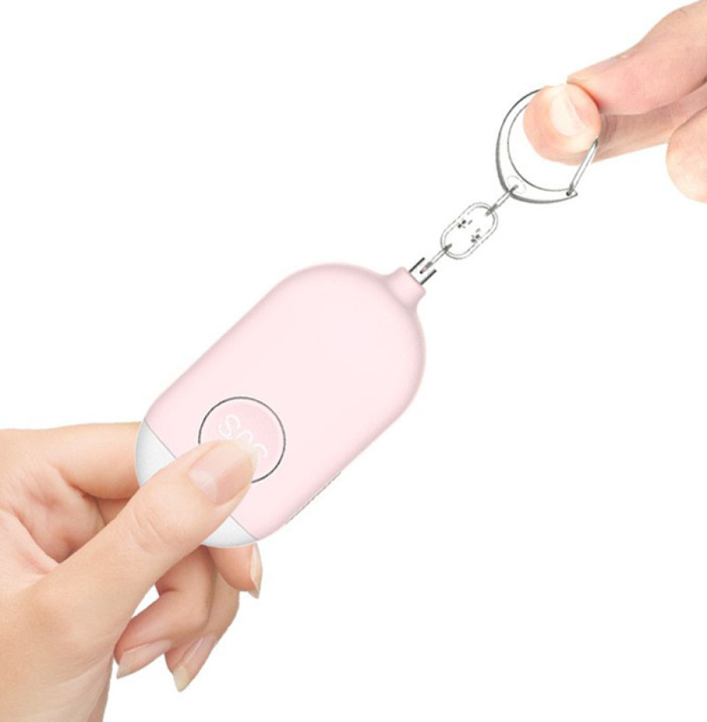 Ein rosa SOS-Schlüsselanhänger wird von zwei Händen gehalten. Eine Hand drückt die SOS-Taste. Eine silberne Kette und ein Ring verbinden das Gerät.