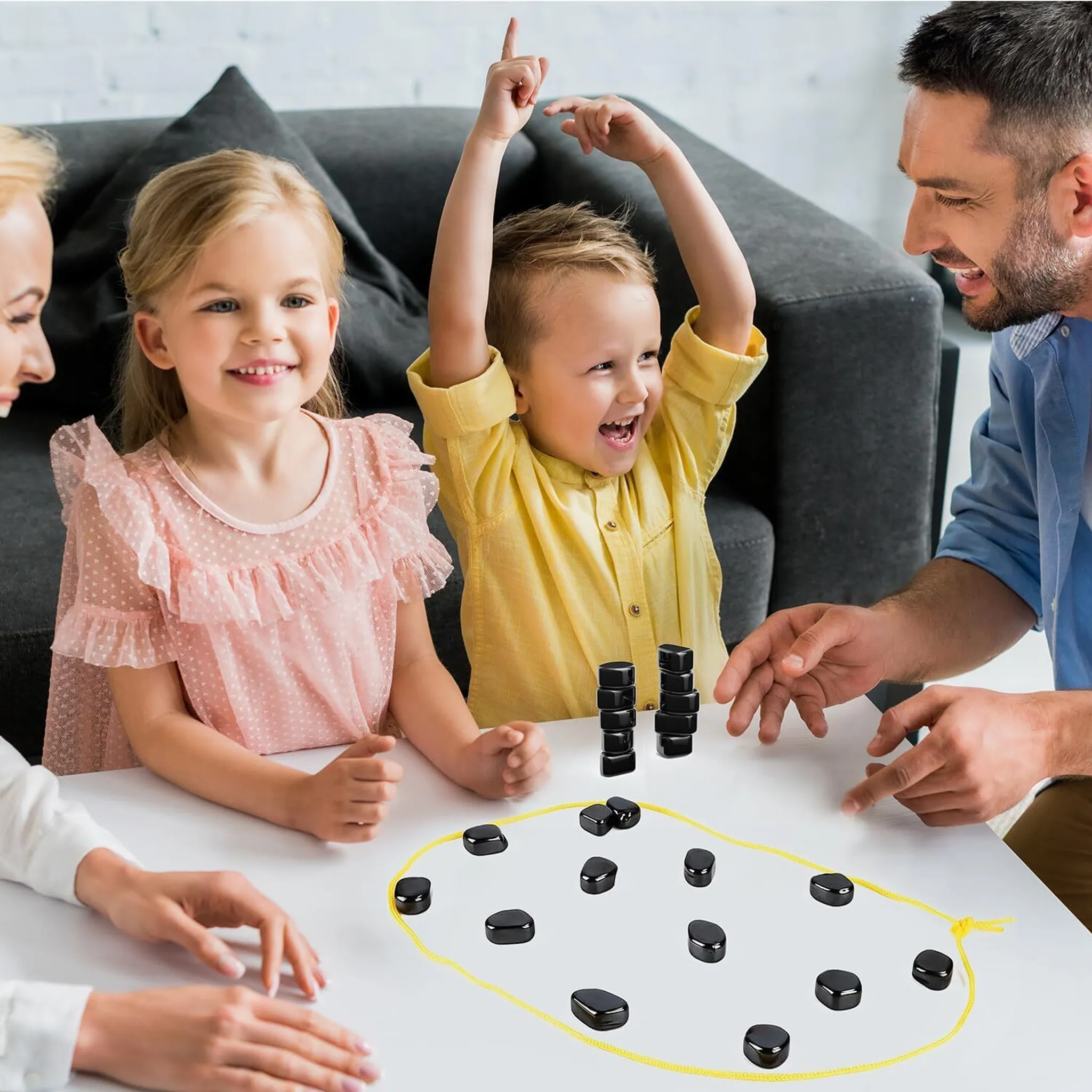 Familie spielt ein Brettspiel. Ein Kind feiert einen Sieg. Schwarze Spielsteine auf einem weißen Tisch. Andere lächeln.