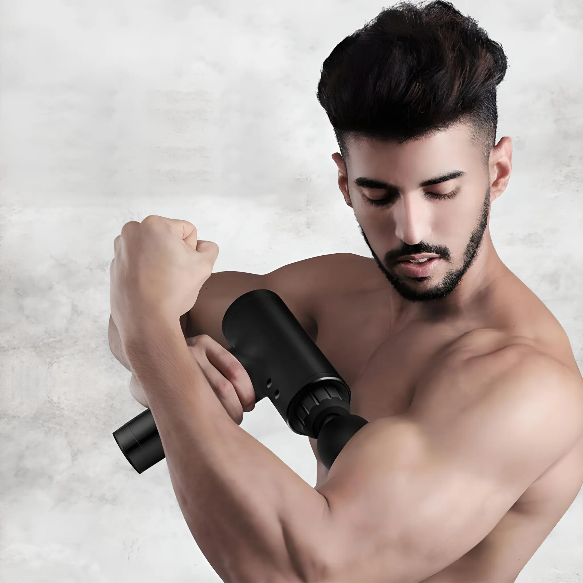 Ein Mann benutzt eine schwarze Massagepistole an seinem Arm. Er hat dunkles Haar, einen Bart und ist oben ohne. Der Hintergrund ist eine Marmorwand.