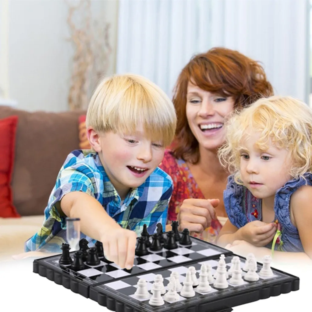 Eine Familie spielt Schach. Ein Junge zieht eine schwarze Figur. Eine Frau und ein anderes Kind schauen lächelnd zu. Das Brett steht auf einem Tisch.
