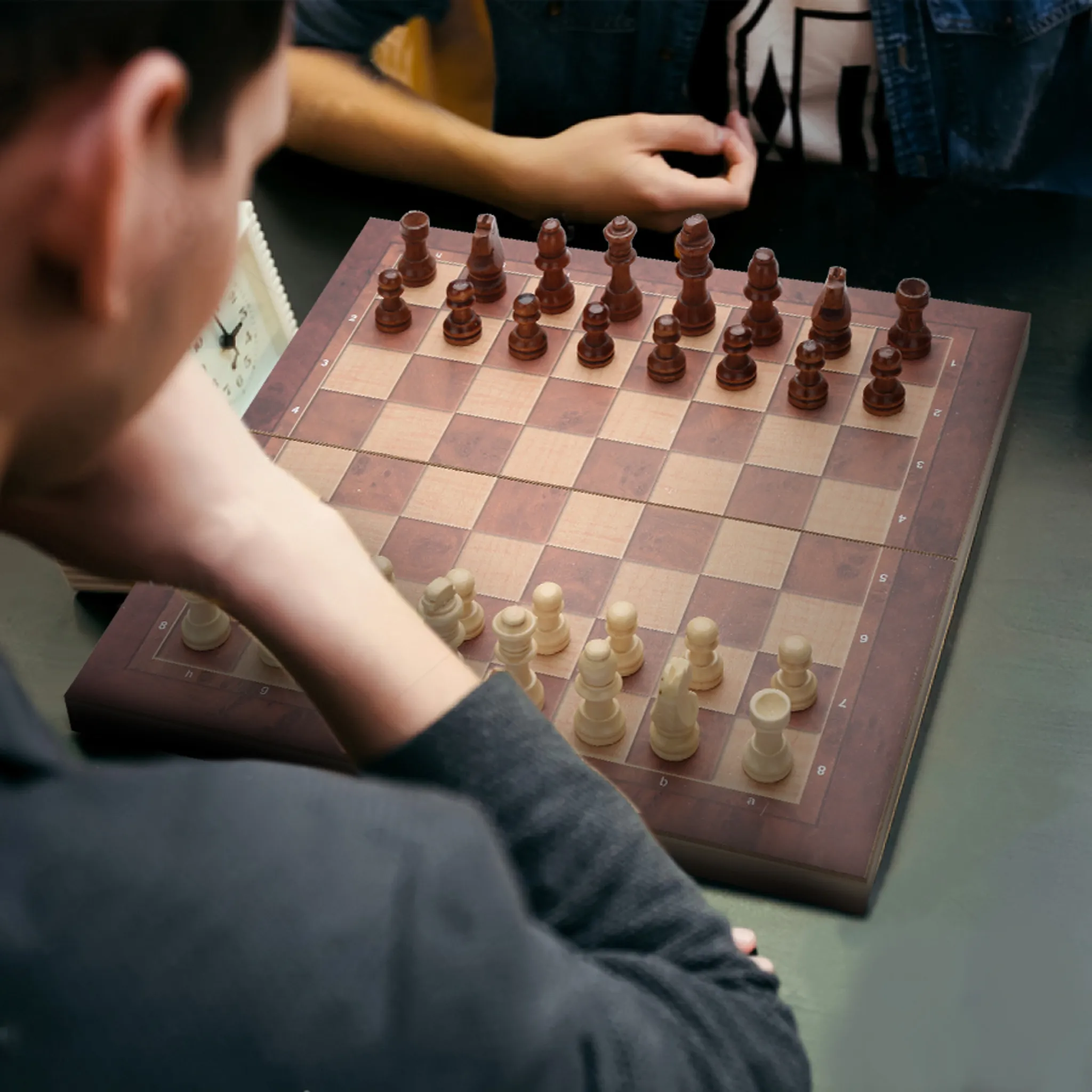 Ein Schachbrett mit Schachfiguren steht zwischen zwei Personen. Eine Person greift nach dem Brett.
