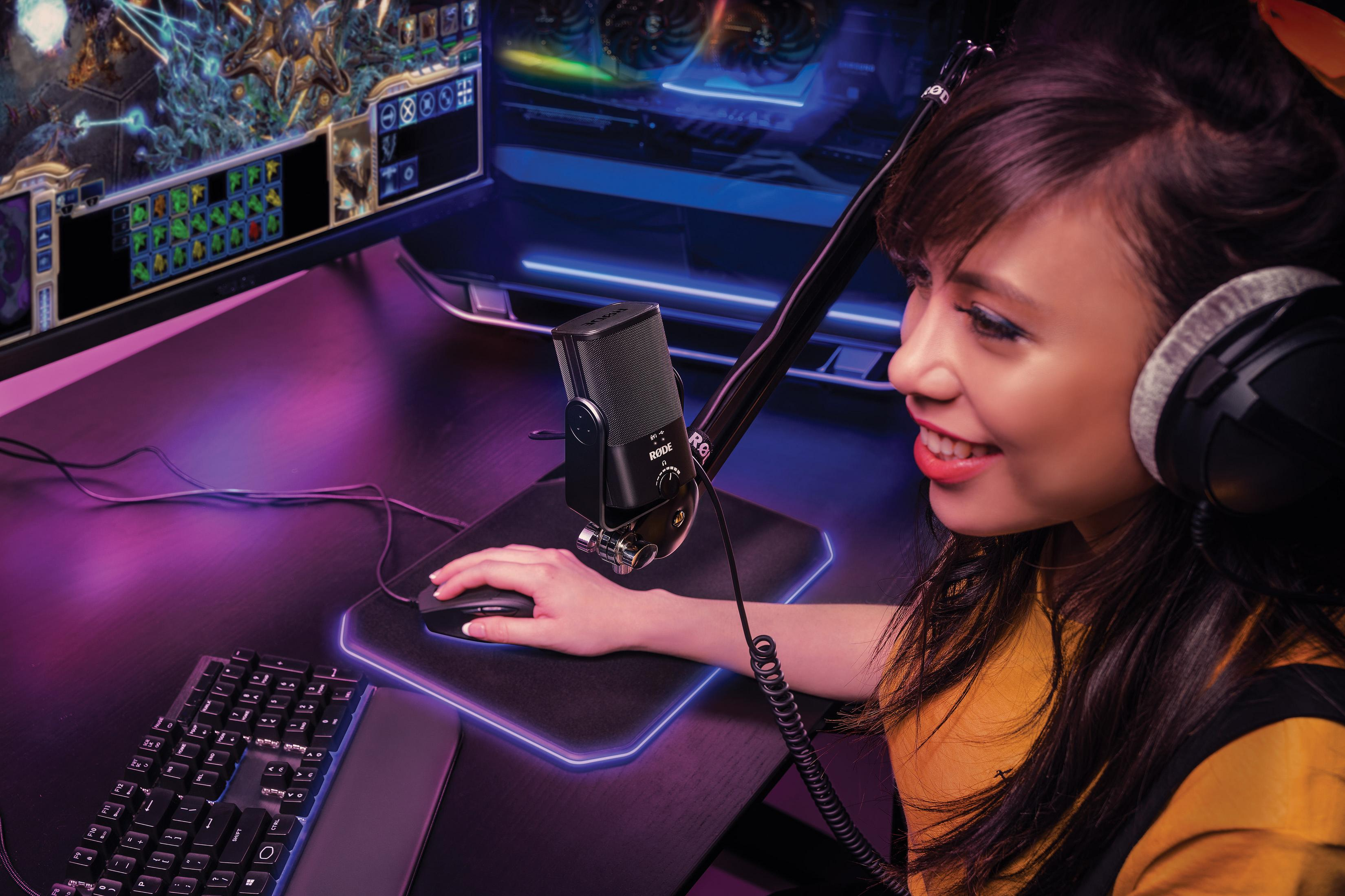 Kobieta ze słuchawkami i mikrofonem gra, z klawiaturą i myszką na fioletowym biurku.