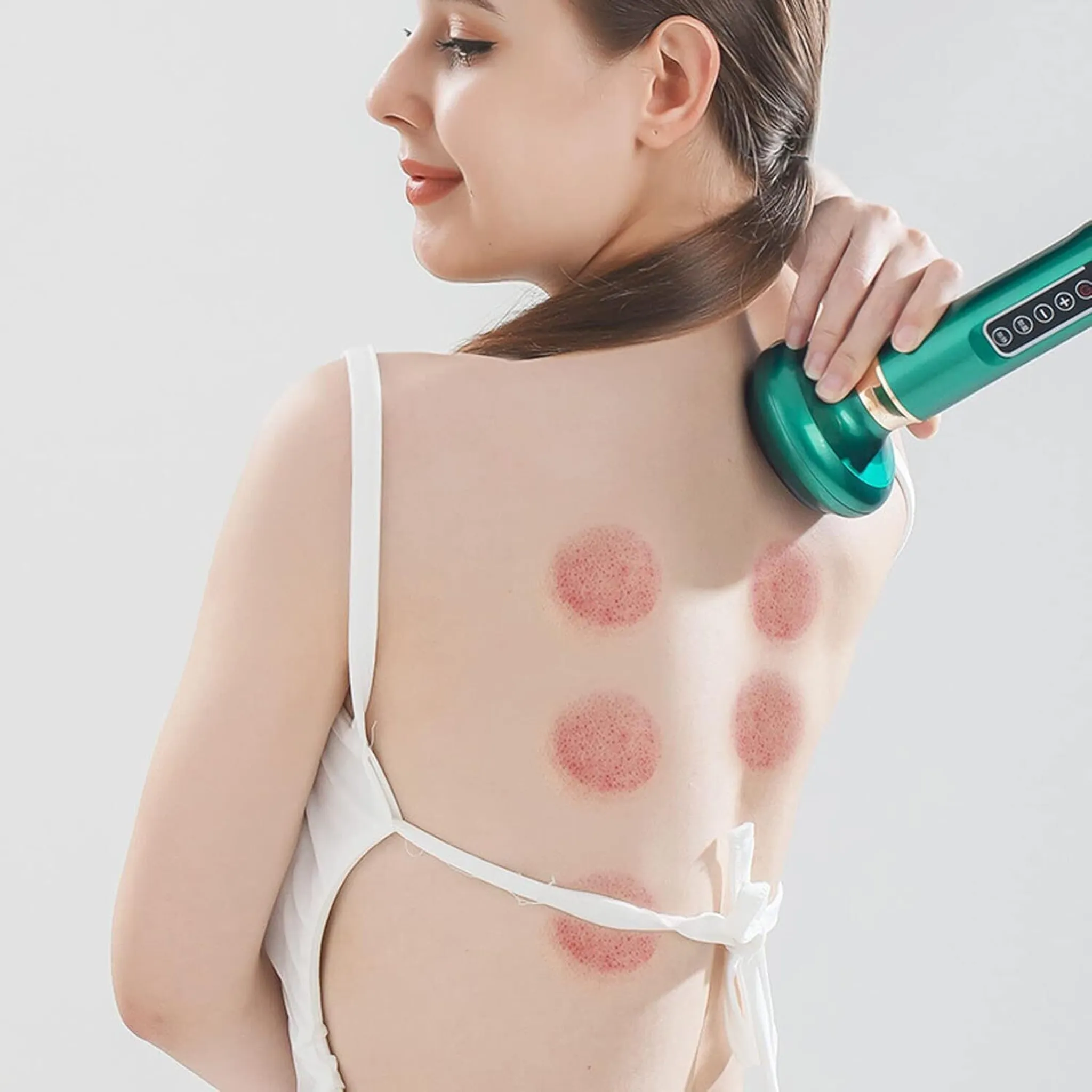 Eine Frau mit Schröpfmalen auf dem Rücken, die ein grünes Massagegerät benutzt. Der Hintergrund ist weiß.