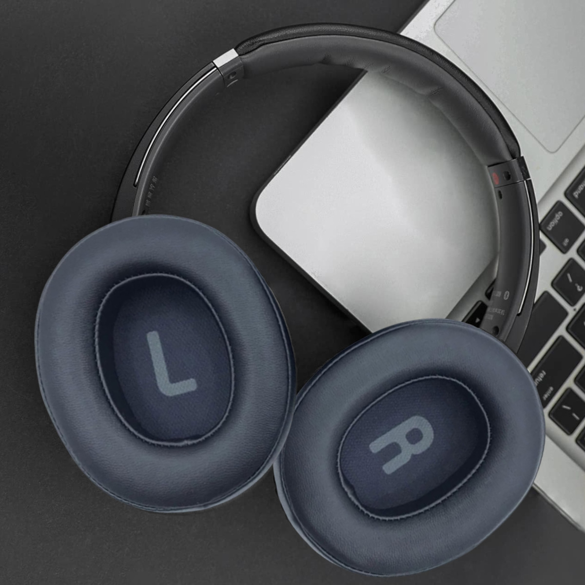 Over-Ear-Kopfhörer mit blauen Ohrmuscheln, die mit 'L' und 'R' gekennzeichnet sind, auf schwarzem Untergrund neben einem Laptop.
