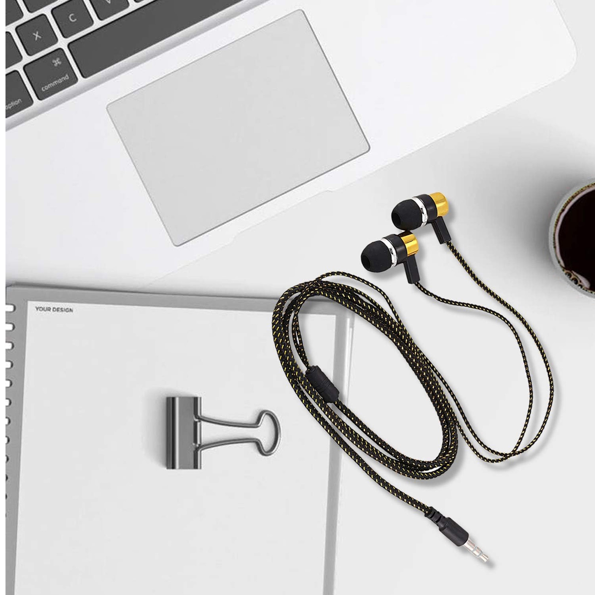 Kopfhörer mit gelb-schwarzem Kabel, eine Büroklammer, Notizbuch, ein Laptop und eine Tasse Kaffee auf einem weißen Schreibtisch.