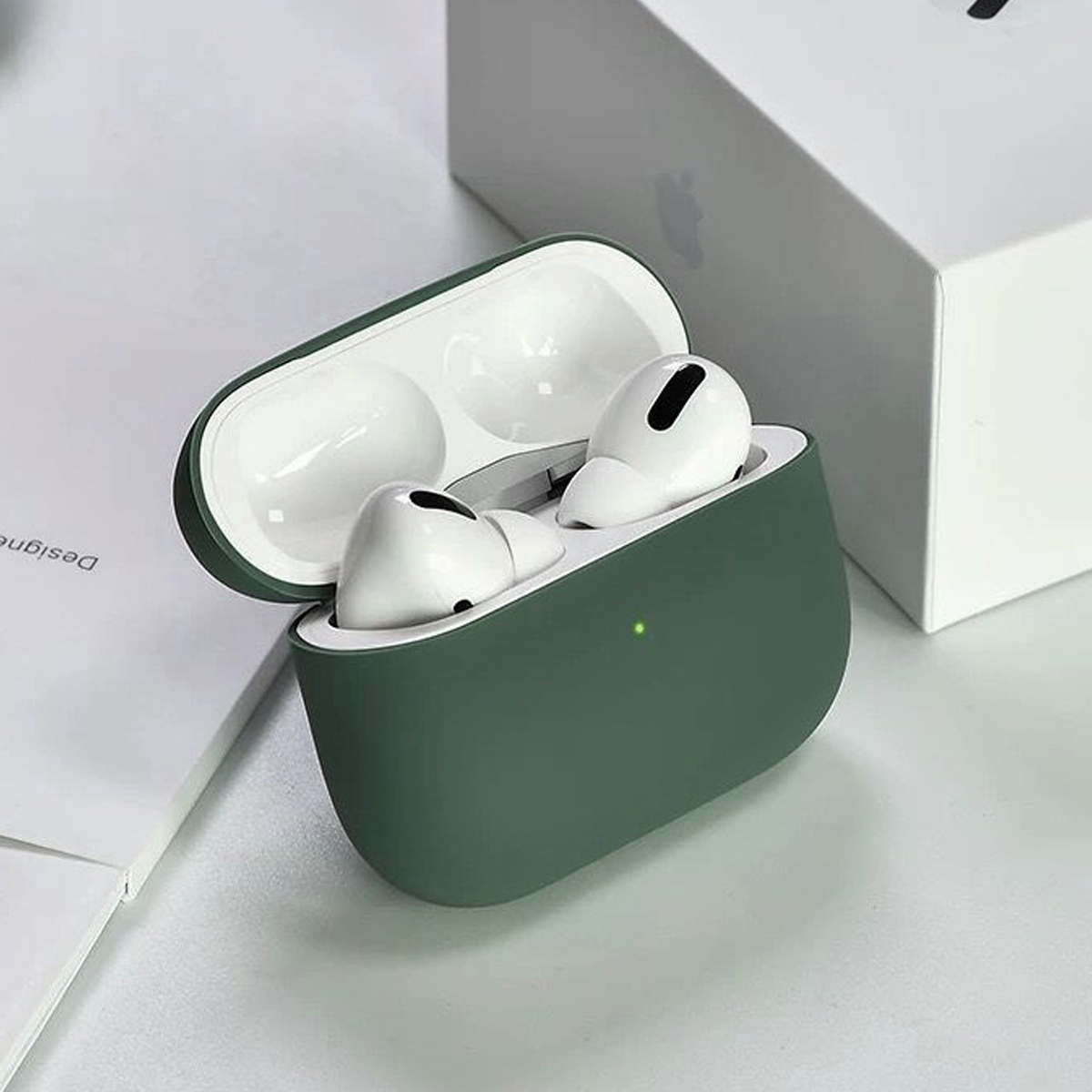 Offene grüne Hülle mit weißen Ohrhörern. Apple-Box im Hintergrund. Weiße Oberfläche. Die Hülle hat ein grünes Licht.