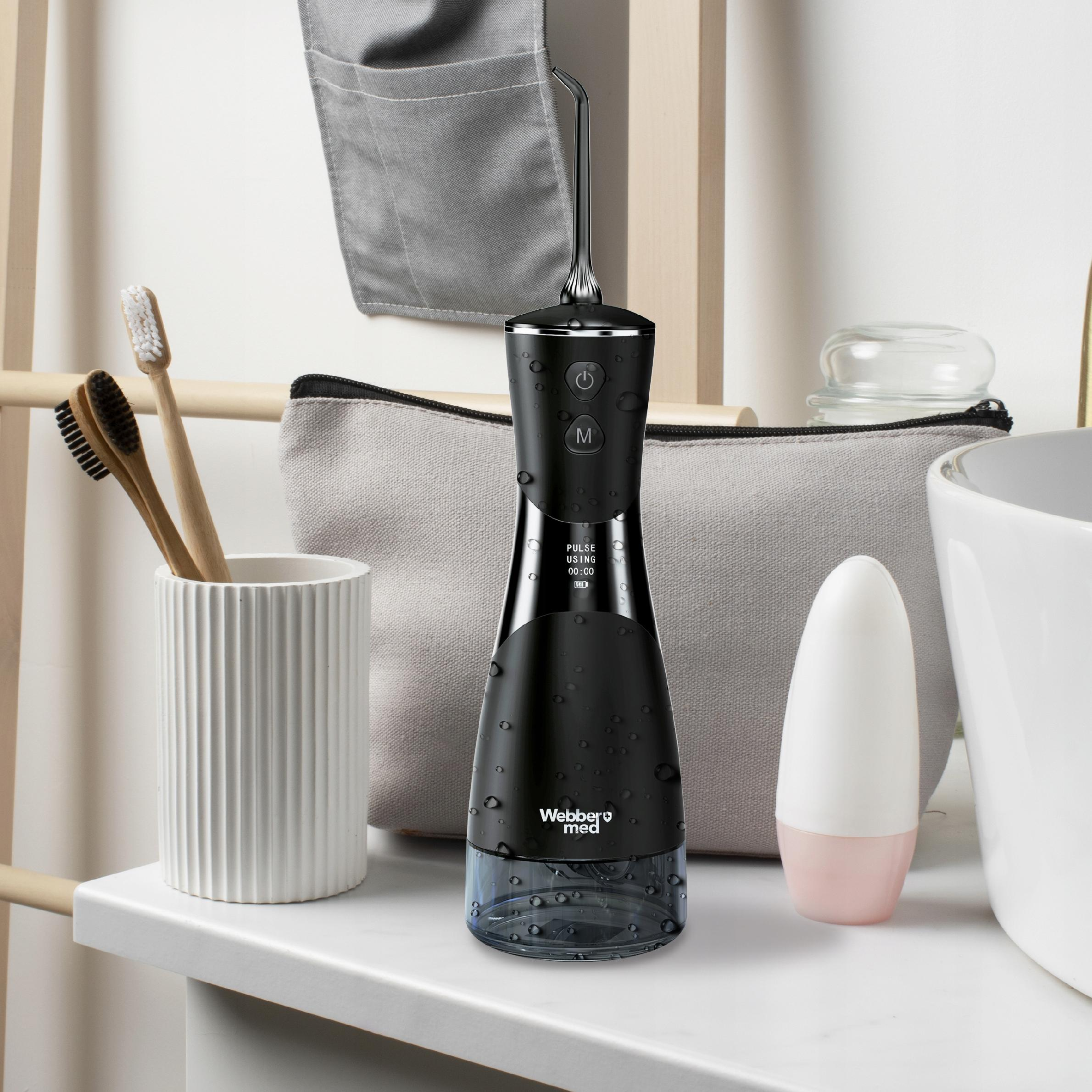 Czarny irygator, szczoteczki do zębów i kosmetyczka na półce. Po prawej stronie biała umywalka.