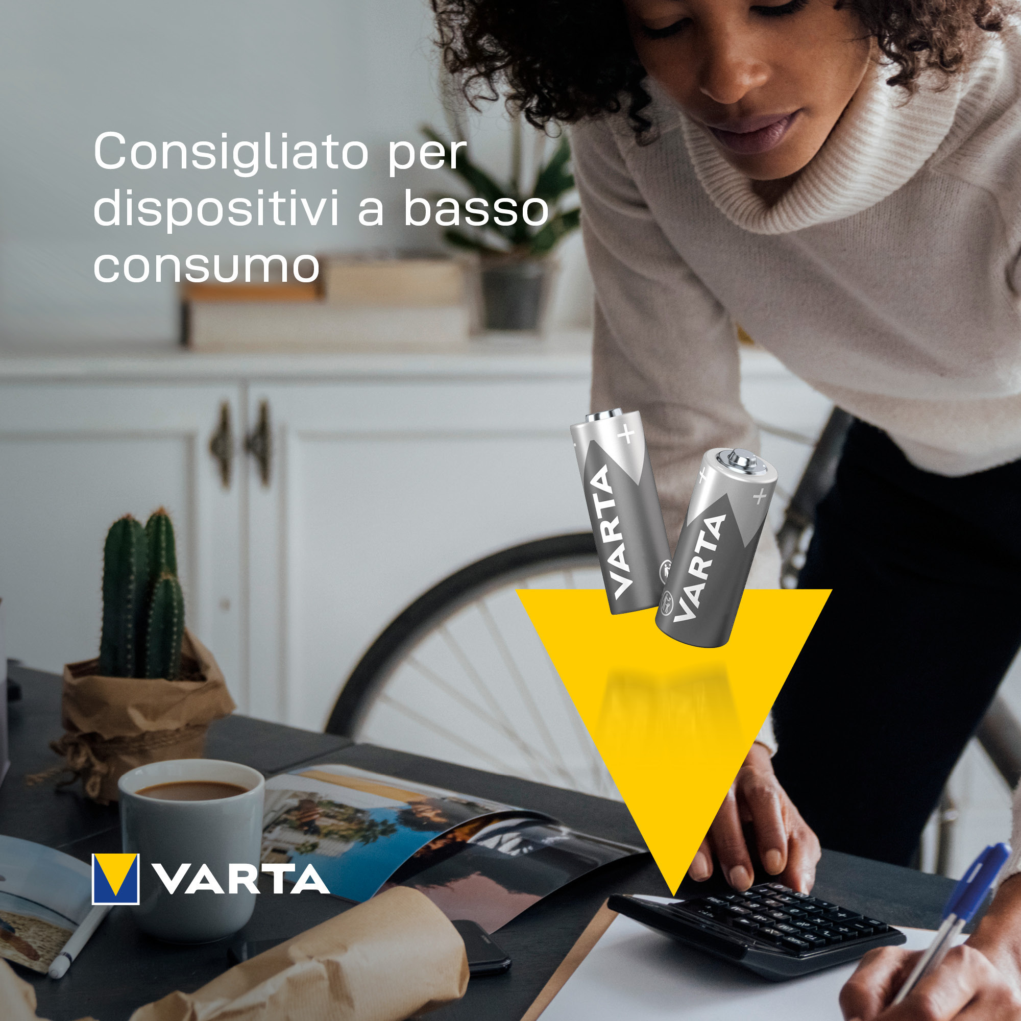 Kobieta pracuje przy biurku z bateriami, kalkulatorem i kawą. Tekst brzmi 'Consigliato per dispositivi a basso consumo'.