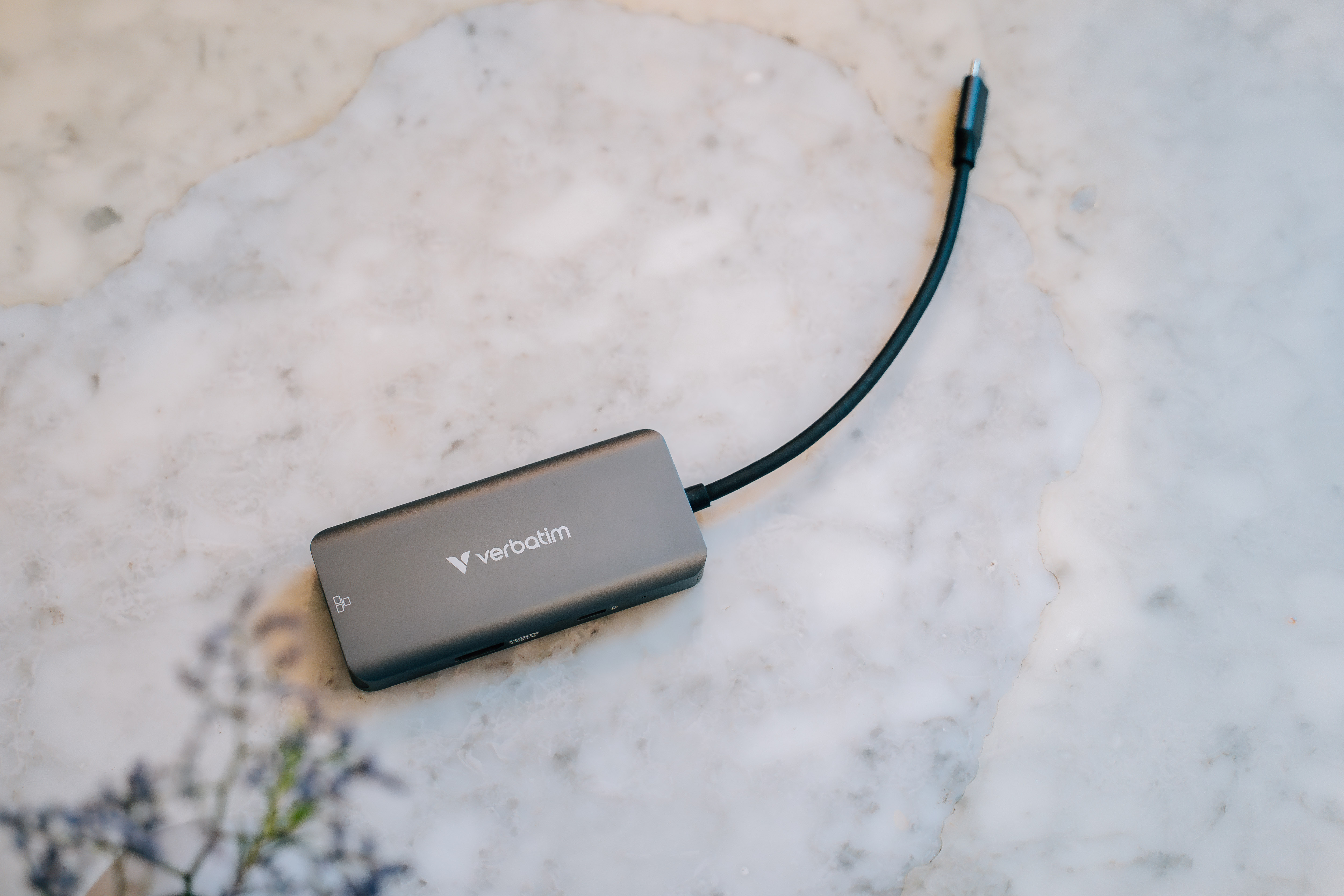 A gray Verbatim USB hub is on a marble surface, connected to a black cable.