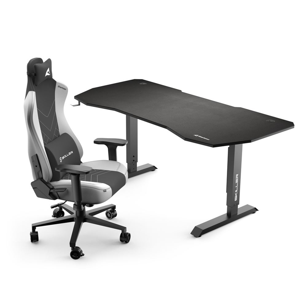 Una configuración de juego con un escritorio negro y una silla de juego gris, blanca y negra. La silla tiene la palabra 'SKILLER'.