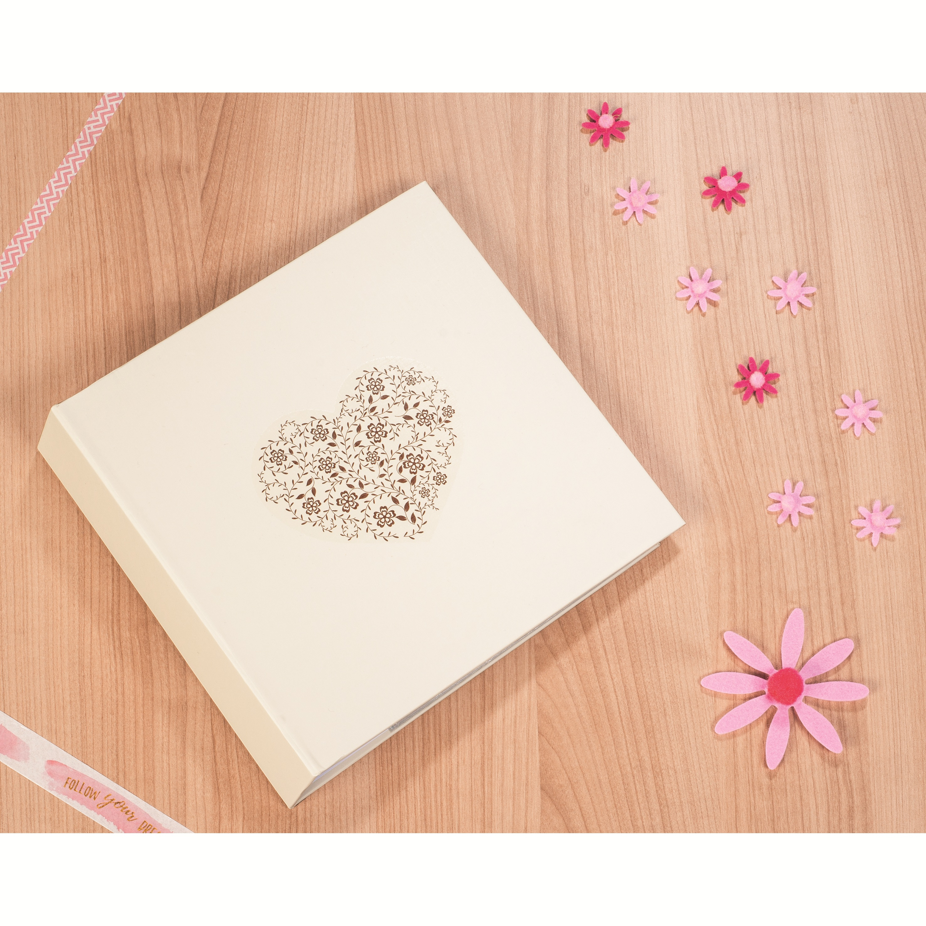Kremowy album z kwiatowym sercem, różowymi kwiatami i dekoracyjną taśmą na drewnianej powierzchni.