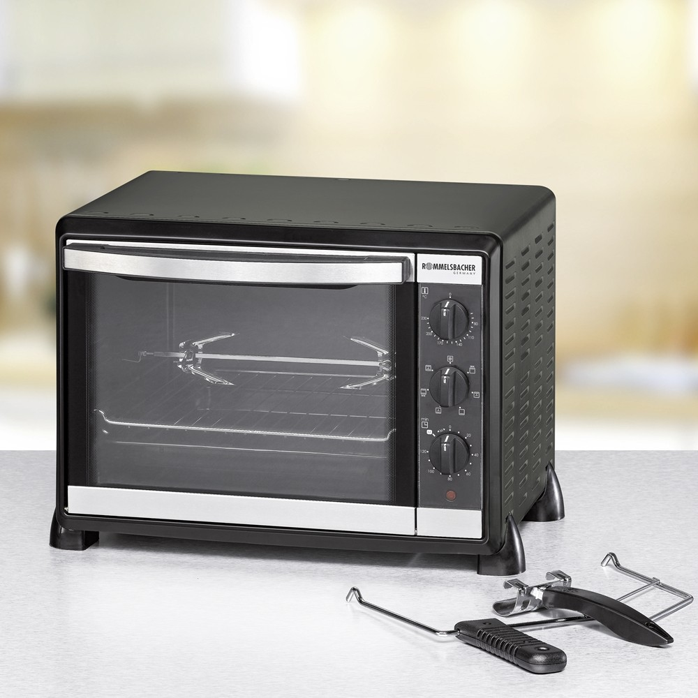 Un forno nero con porta a vetri, comandi a destra e accessori davanti. Lo sfondo è sfocato con un colore chiaro.
