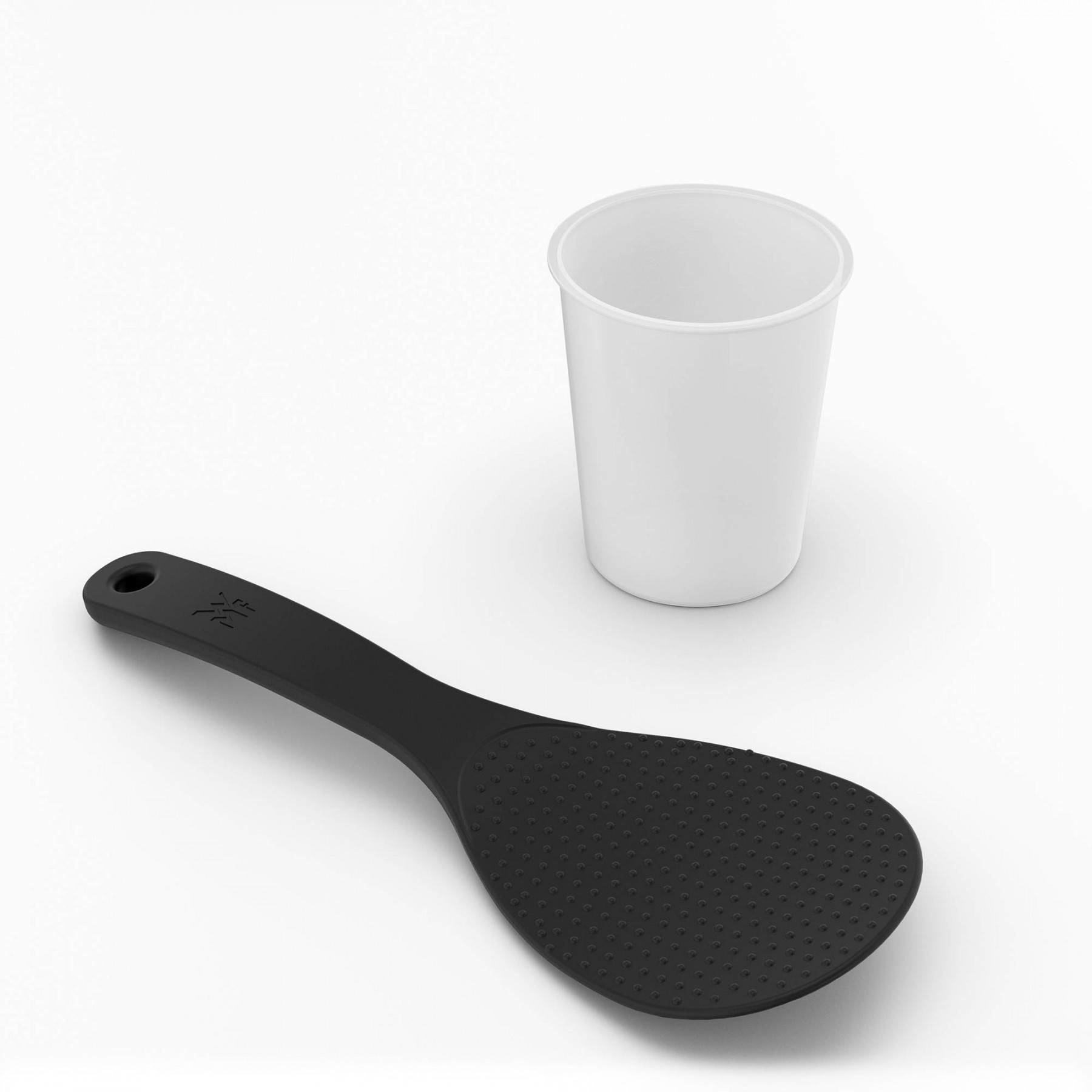 Una paleta de arroz negra y una taza blanca están sobre una superficie blanca. La paleta está a la izquierda y la taza a la derecha.
