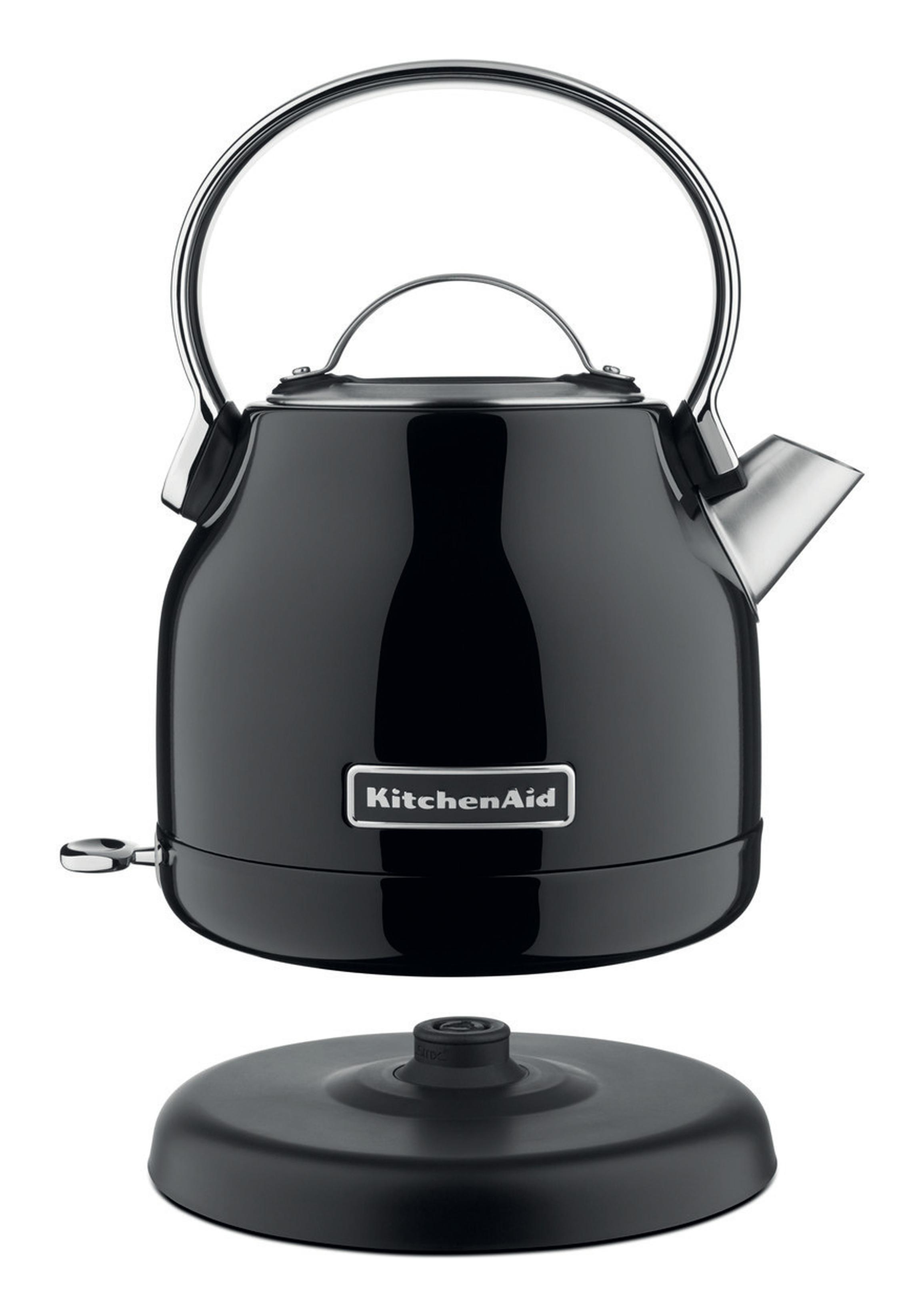 Een zwarte KitchenAid waterkoker met zilveren handvat en tuit staat bovenop zijn zwarte voet, geïsoleerd op wit.
