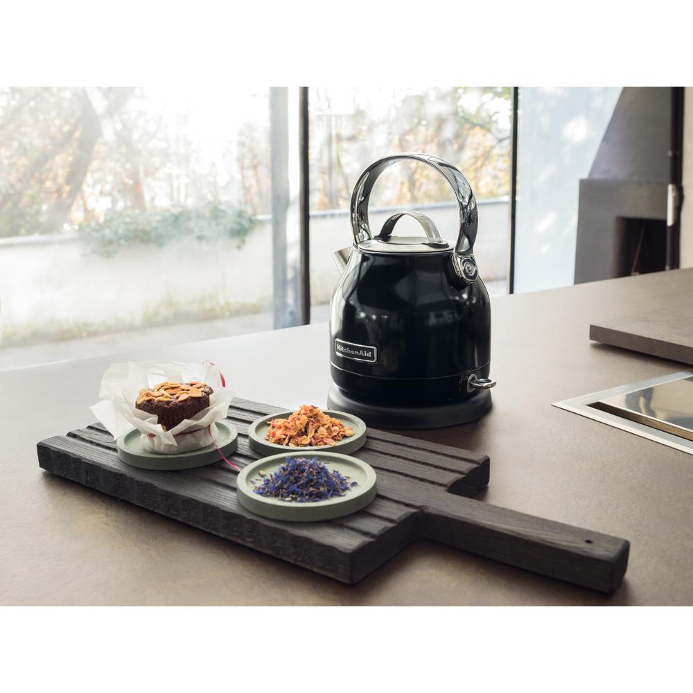 Een zwarte KitchenAid waterkoker, een houten dienblad met cake en kruiden, op een bruin aanrecht. Raam op de achtergrond.