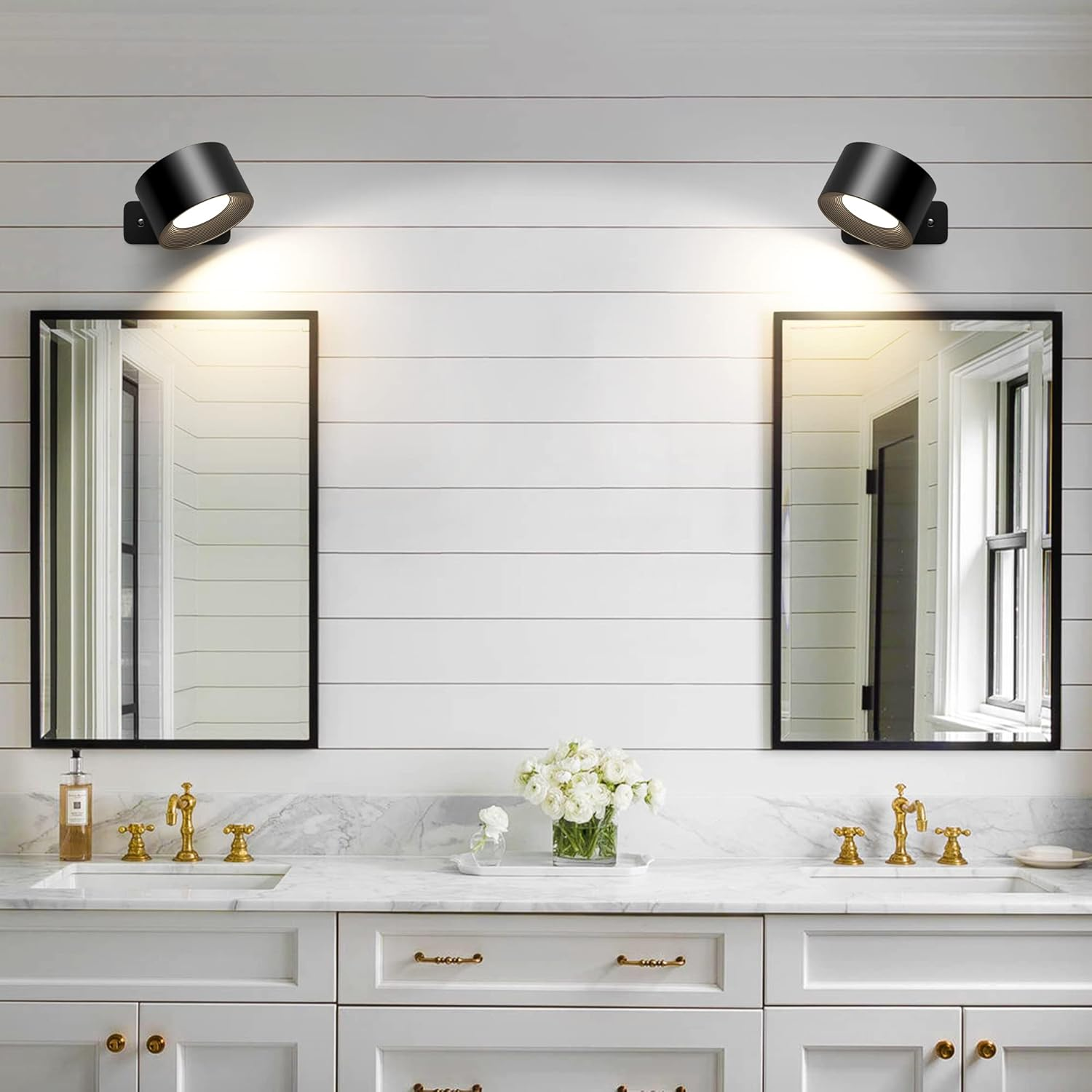 Badezimmer mit weißen Wänden, Spiegeln und Doppelwaschbecken. Schwarze Strahler über den Spiegeln. Goldene Wasserhähne und weiße Schränke.