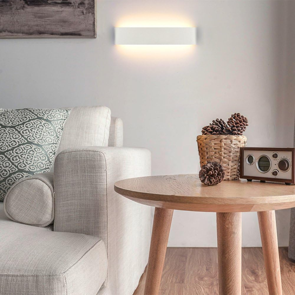 Ein modernes Wohnzimmer mit weißem Sofa, rundem Holztisch und Wandlampe. Ein Korb mit Tannenzapfen und ein Radio stehen auf dem Tisch.