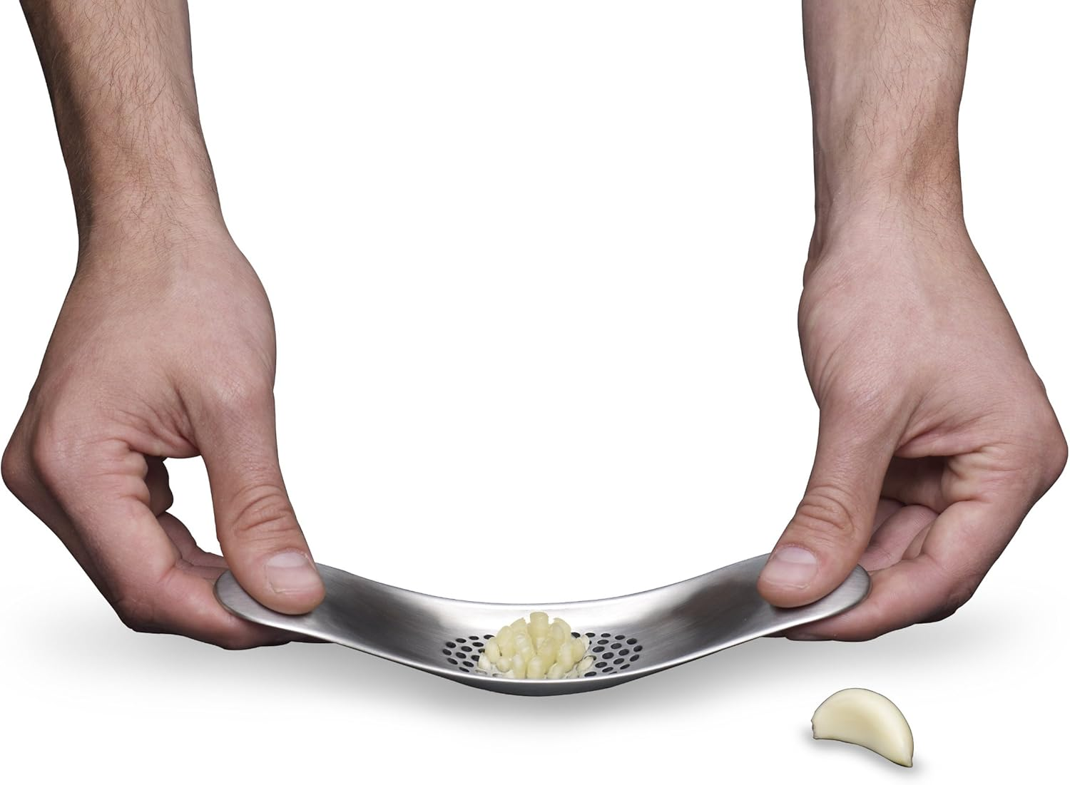 Hände halten eine Knoblauchpresse mit gehacktem Knoblauch darin und einer Knoblauchzehe daneben. Die Presse ist silberfarben.