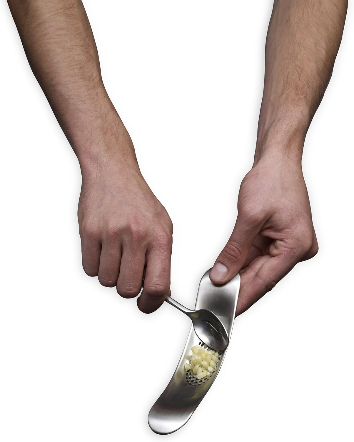 Hände benutzen eine Knoblauchpresse. Gehackter Knoblauch befindet sich darin, und ein kleiner Löffel wird verwendet, um den Knoblauch durchzudrücken.