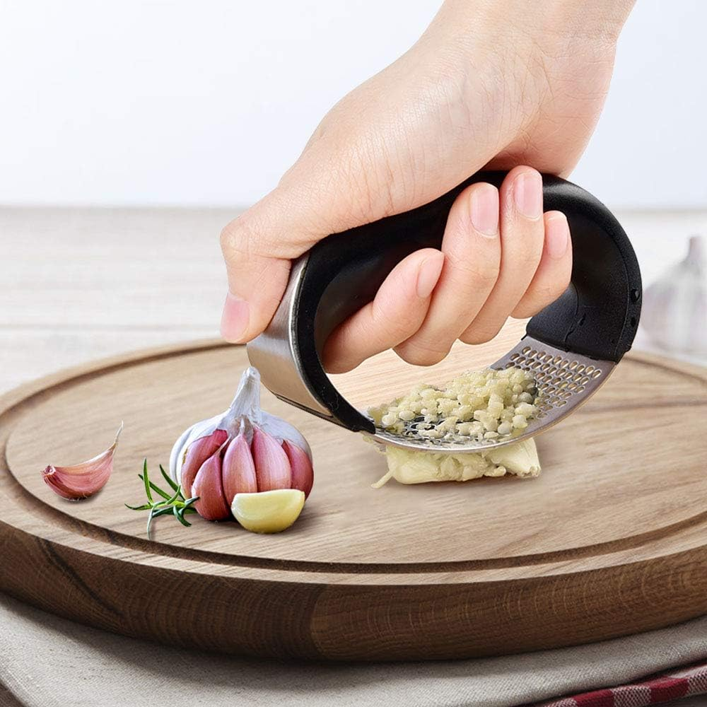 Eine Hand betätigt eine Knoblauchpresse. Gehackter Knoblauch kommt auf einem Schneidebrett zum Vorschein. Knoblauchzehen und -knolle sind sichtbar.