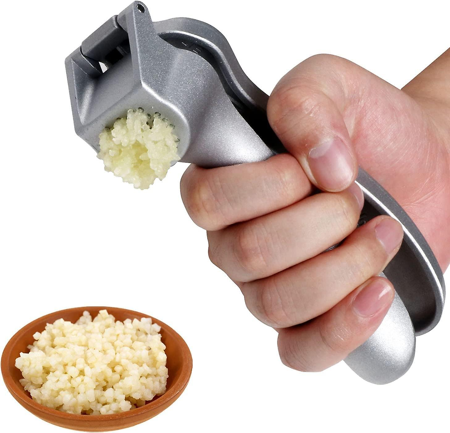 Eine Hand drückt eine Knoblauchpresse und extrudiert gehackten Knoblauch. Eine kleine Schüssel mit gehacktem Knoblauch steht darunter.