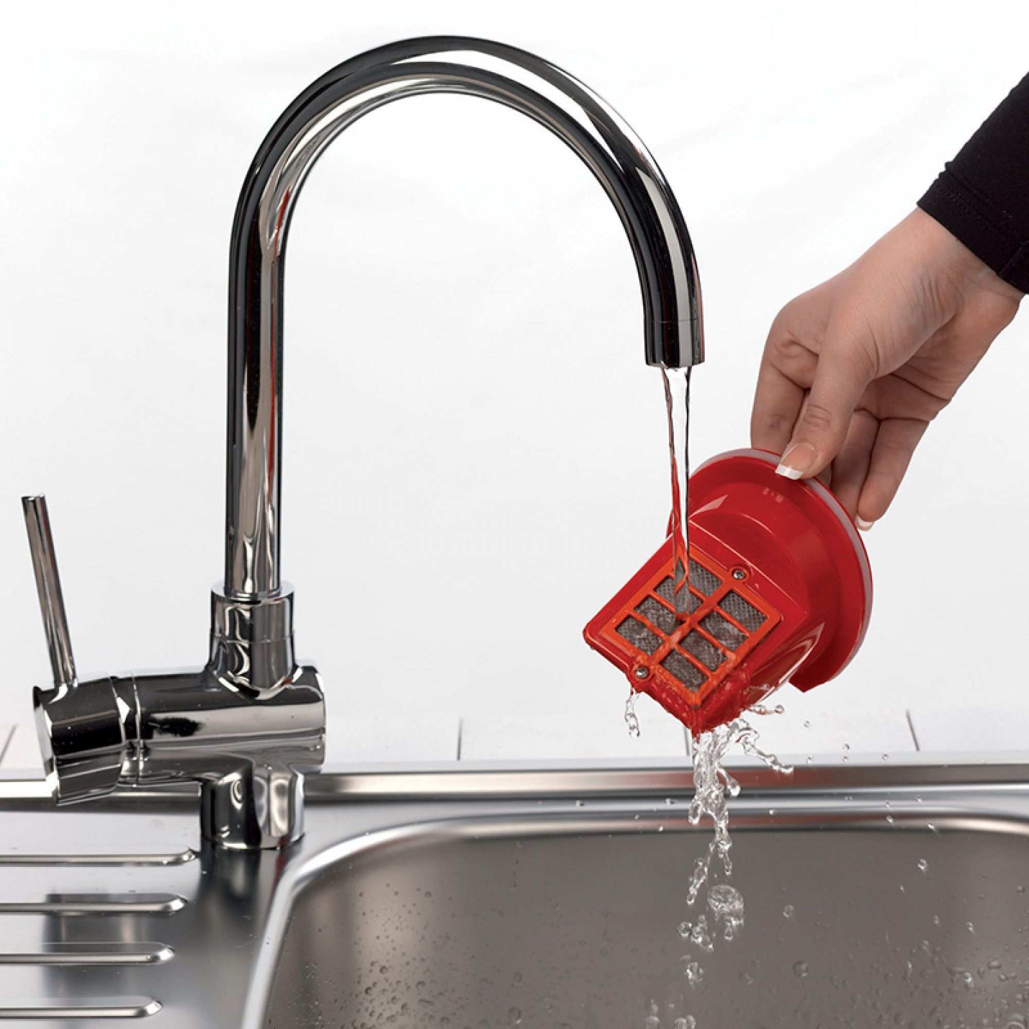 A hand washes a red filter under a chrome faucet. Water streams from the faucet onto the filter, over a silver sink.