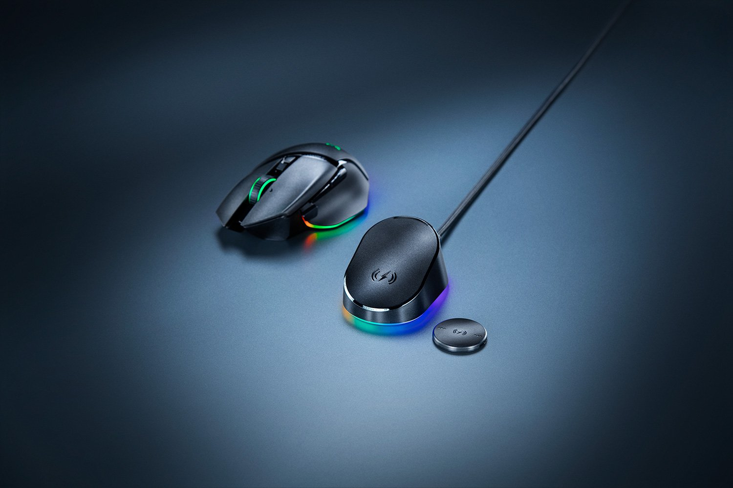 Eine schwarze Gaming-Maus, eine Ladestation und ein Puck mit RGB-Beleuchtung auf dunkler Oberfläche. Ein Kabel verbindet die Dockingstation.
