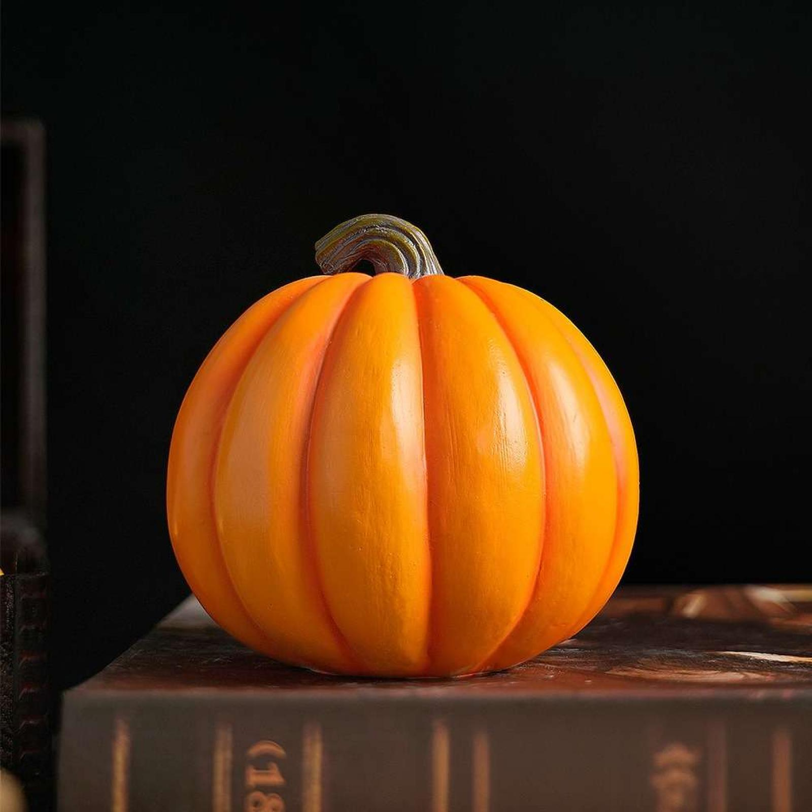 Ein orangefarbener Kürbis mit grünem Stiel liegt auf einem braunen Buch vor dunklem Hintergrund.
