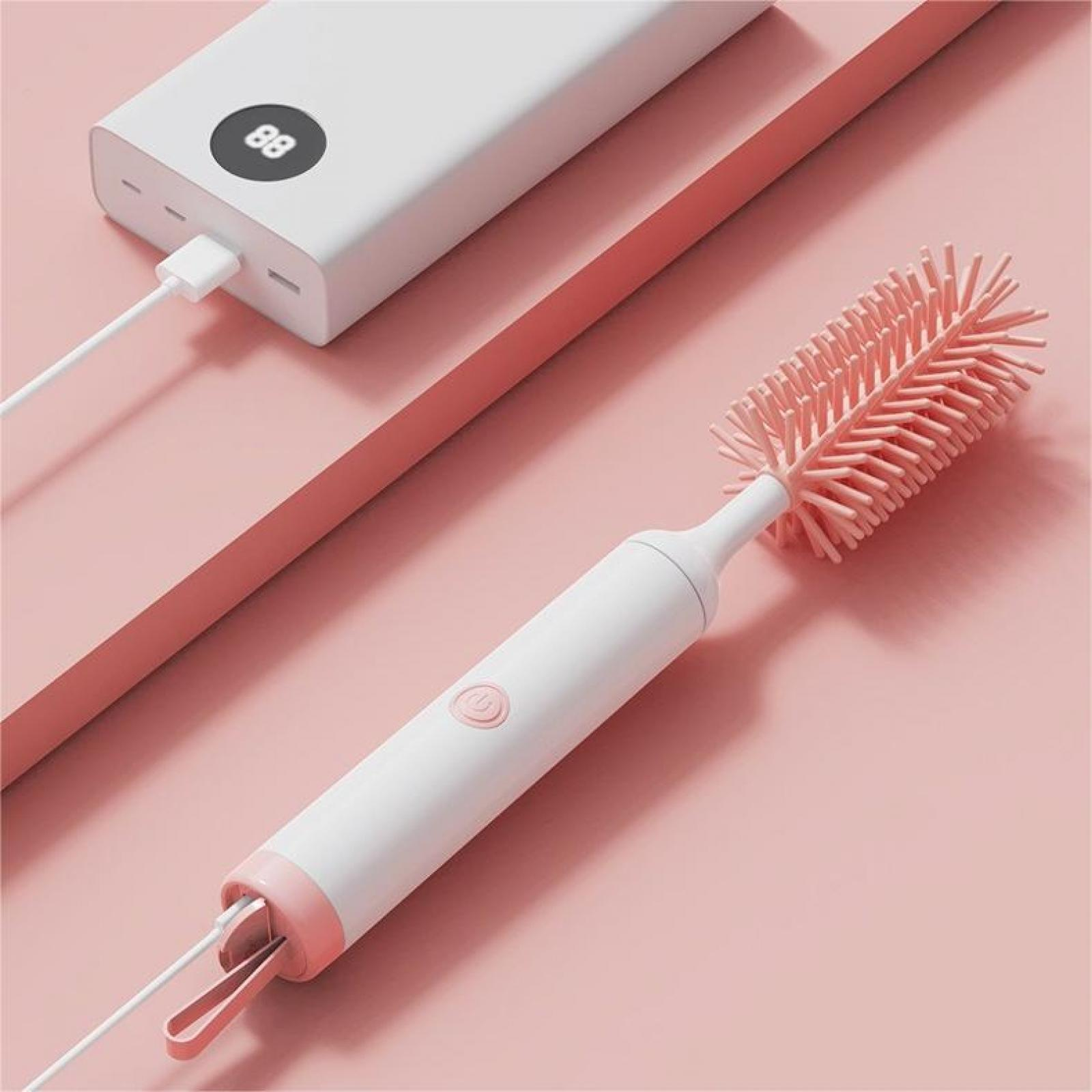 Eine weiße und rosa Reinigungsbürste neben einer weißen Powerbank mit Ladekabel auf rosa Oberfläche.