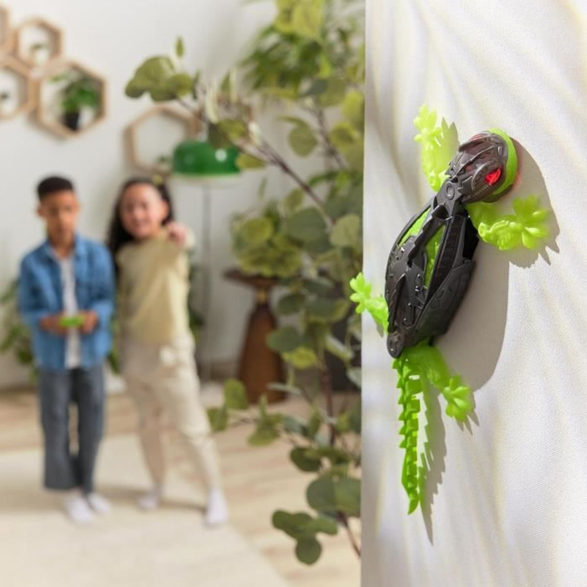 Un insecto de juguete está adherido a una pared. Dos niños están al fondo. El insecto es negro y verde.