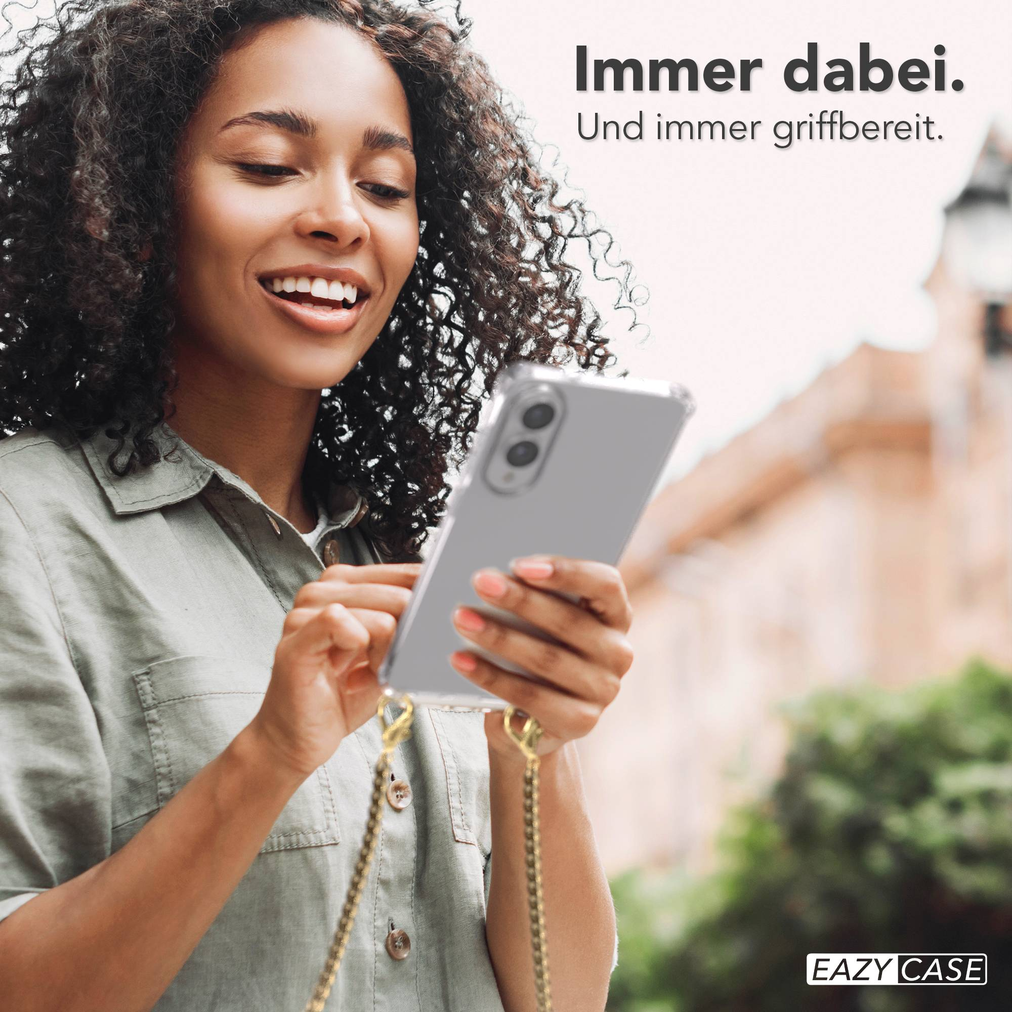 Eine Frau hält lächelnd ein Telefon mit Hülle. Im Hintergrund ein Gebäude und Text: 'Immer dabei'.