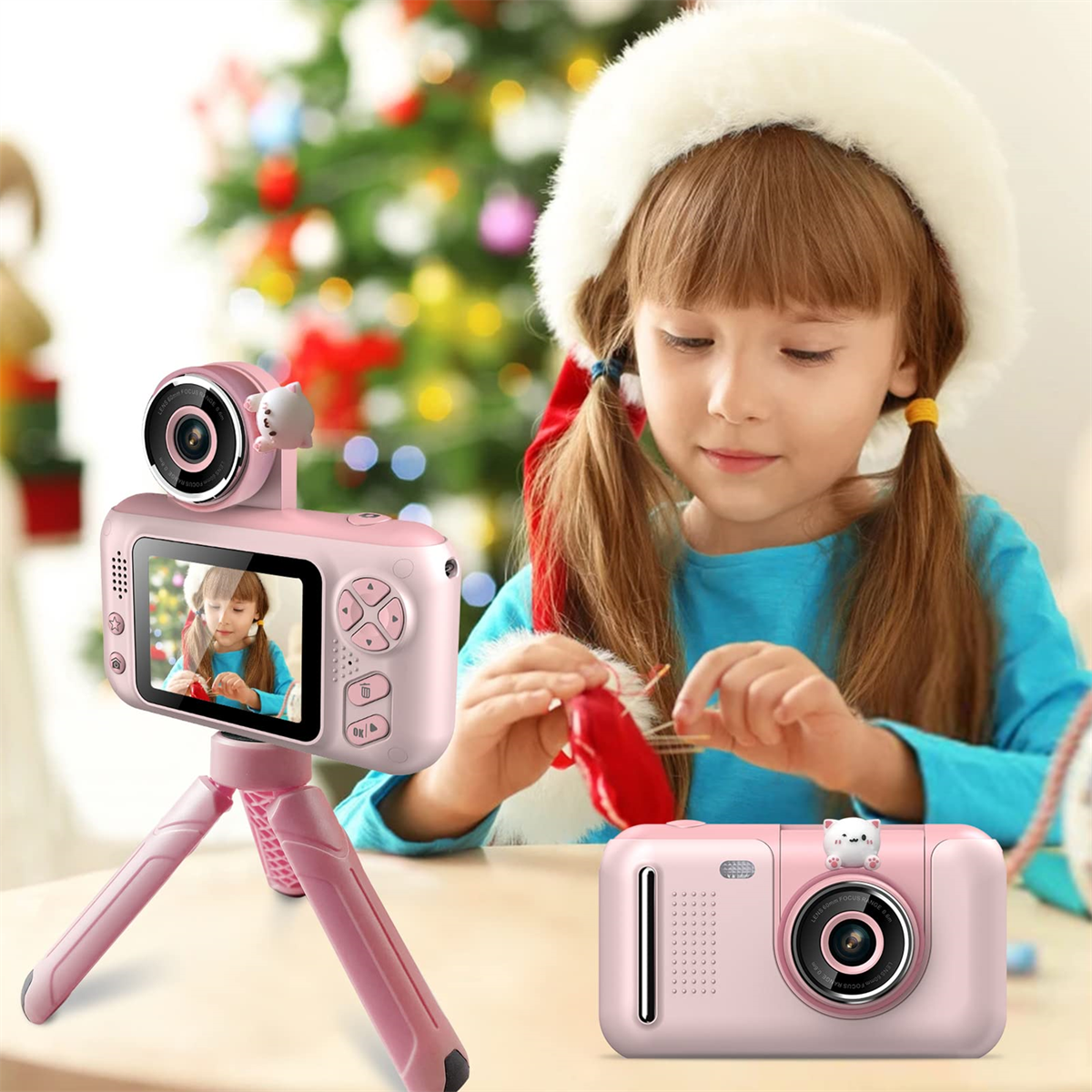Ein Mädchen mit Weihnachtsmütze hält einen roten Gegenstand. Eine rosa Kamera steht auf einem Stativ und eine weitere auf dem Tisch.
