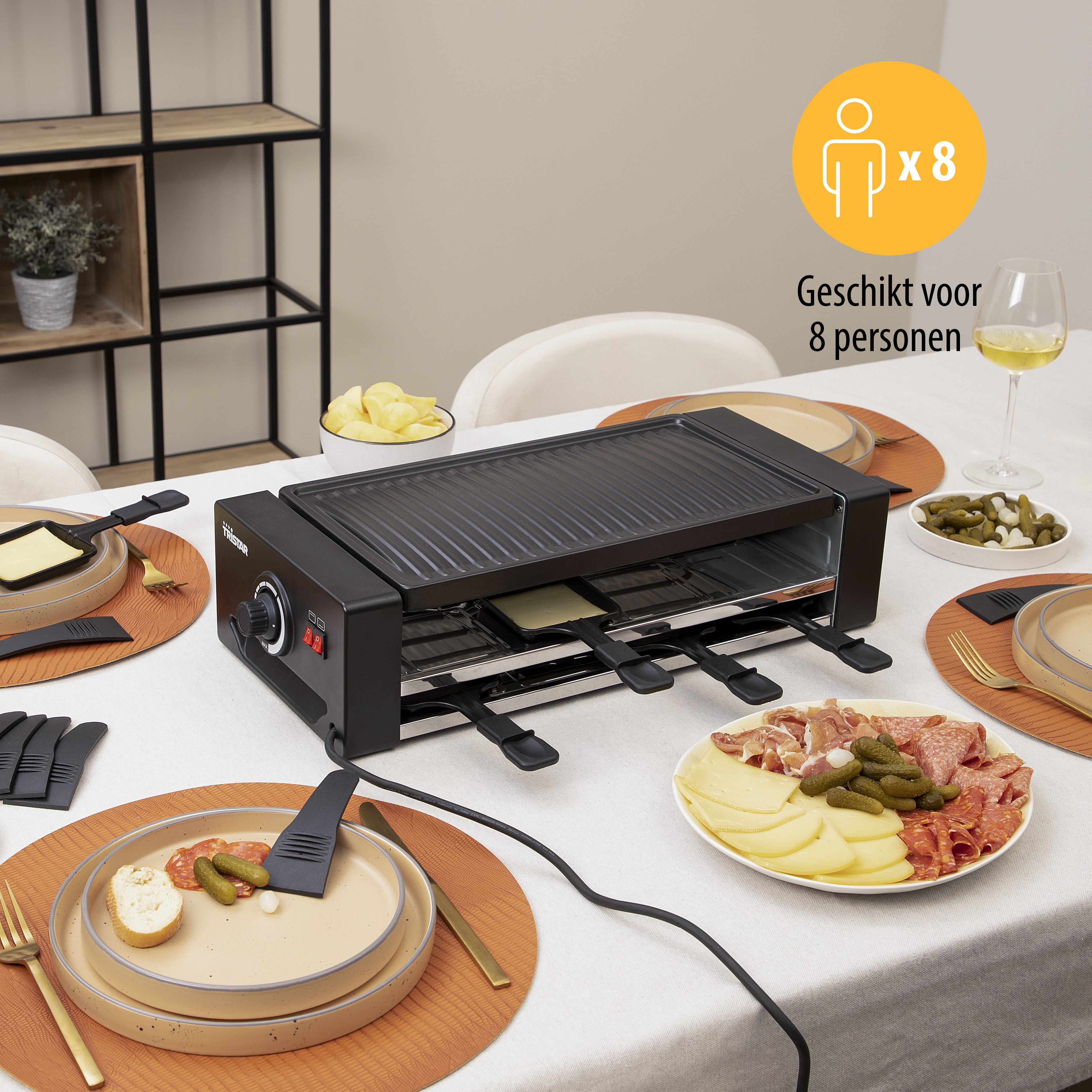 Grill do raclette z jedzeniem, talerzami i sztućcami na posiłek. Scena rozgrywa się na stole.