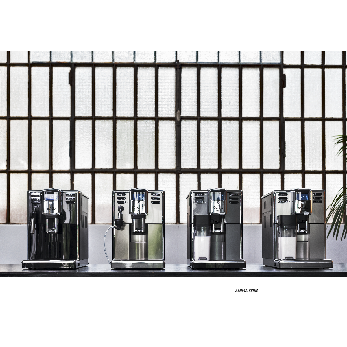 Cztery ekspresy do kawy są wystawione na stole. Tło przedstawia okno z wzorem kratki. Maszyny są w różnych kolorach.