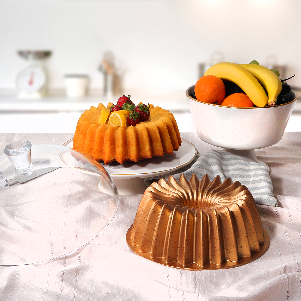 Una mesa muestra un pastel, fruta y un molde para pastel. El pastel está cubierto con fresas y rodajas de limón.