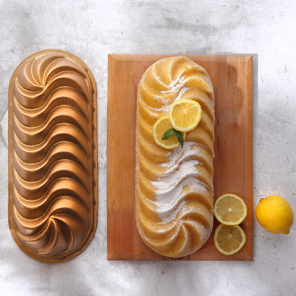 Un pastel de limón horneado con rodajas de limón y azúcar en polvo, un molde para pastel y un limón entero sobre la mesa.