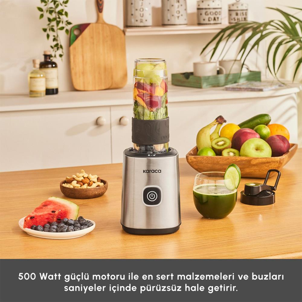 İçinde meyveler olan bir blender, bir bardak meyve suyu ve ahşap bir masada bir kase meyve. Bir dilim karpuz ve kuruyemişler de mevcut.