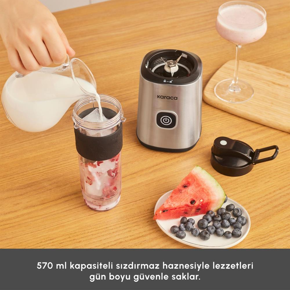 Bir el, bir blender kabına süt döküyor. Ahşap yüzeyde bir smoothie bardağı, blender, karpuz ve yaban mersini de var.