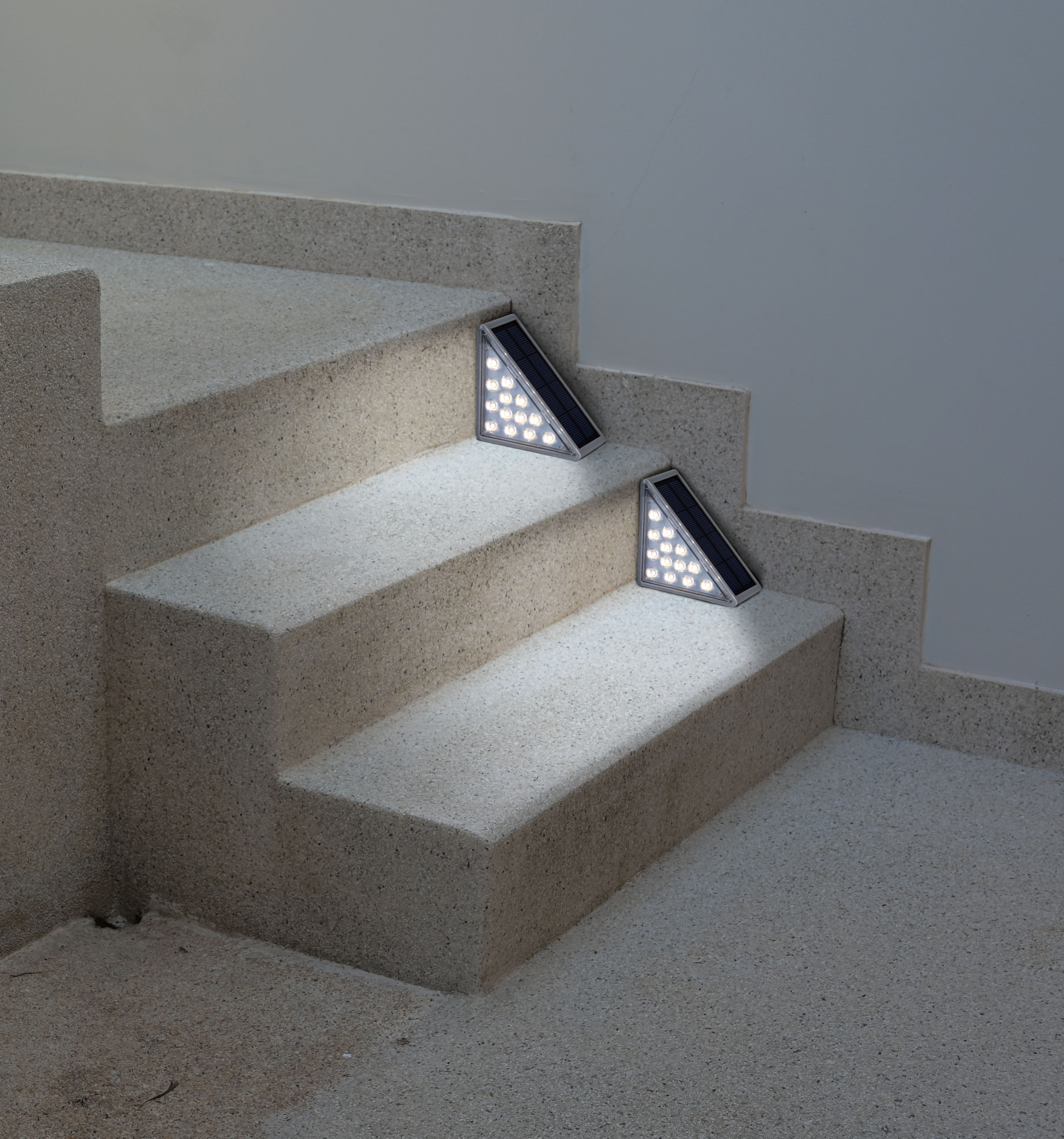 Treppe mit zwei dreieckigen LED-Leuchten auf den Stufen. Die Stufen sind hellbeige. Im Hintergrund ist eine hellgraue Wand.