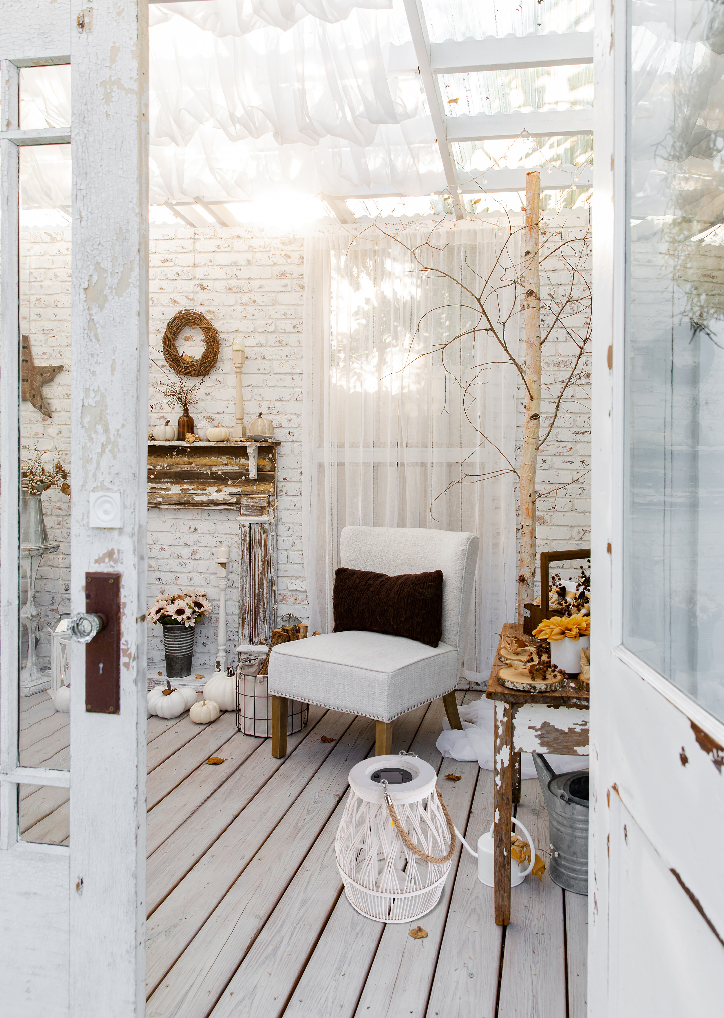 Ein weißes Zimmer mit Stuhl, Kürbissen und einem Baum. Weiße Backsteinmauern, transparente Vorhänge und Holzboden sichtbar.
