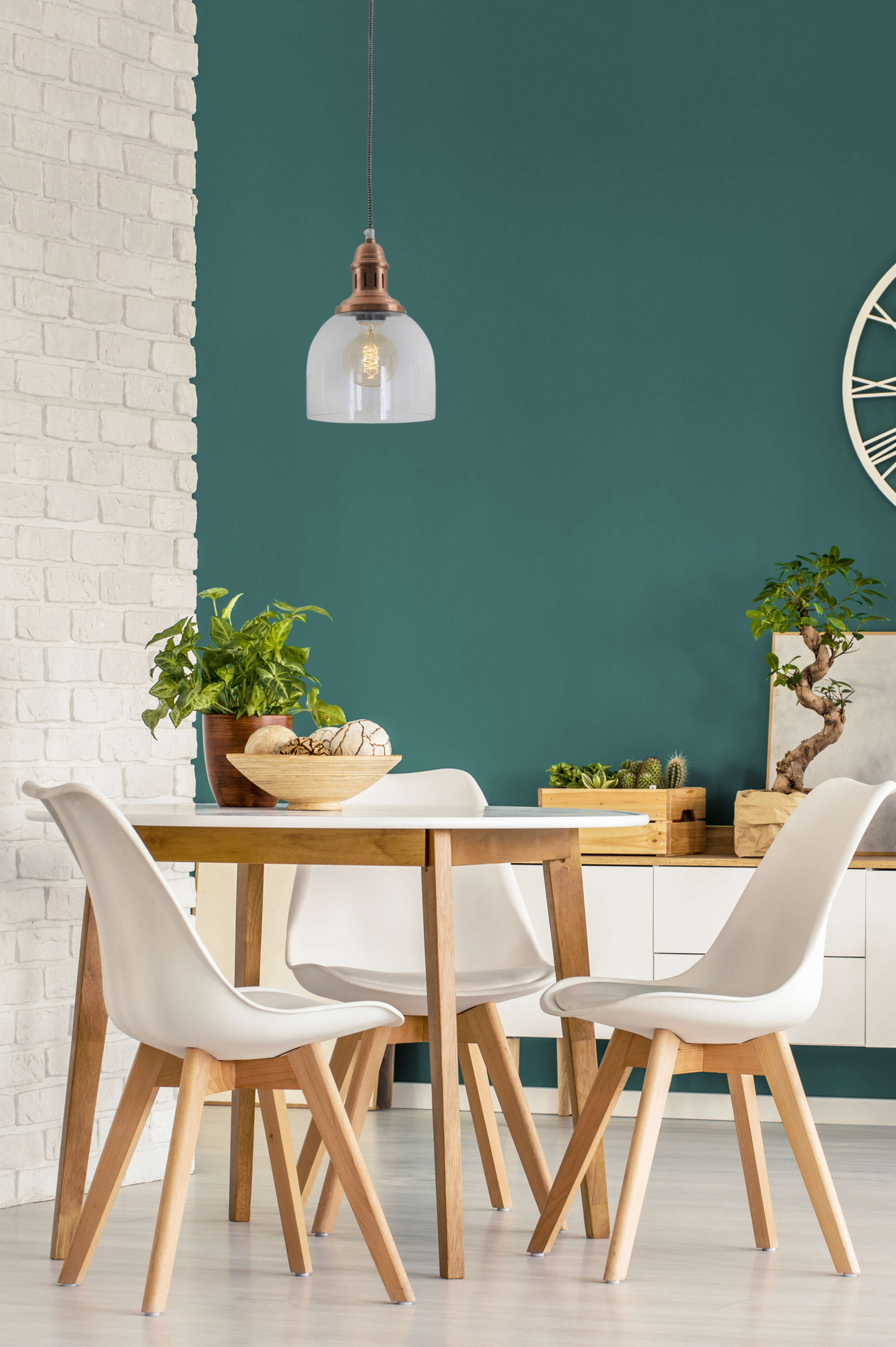Ein Esszimmer mit weißen Stühlen, einem Holztisch und einer grünen Wand. Über dem Tisch hängt eine Lampe.
